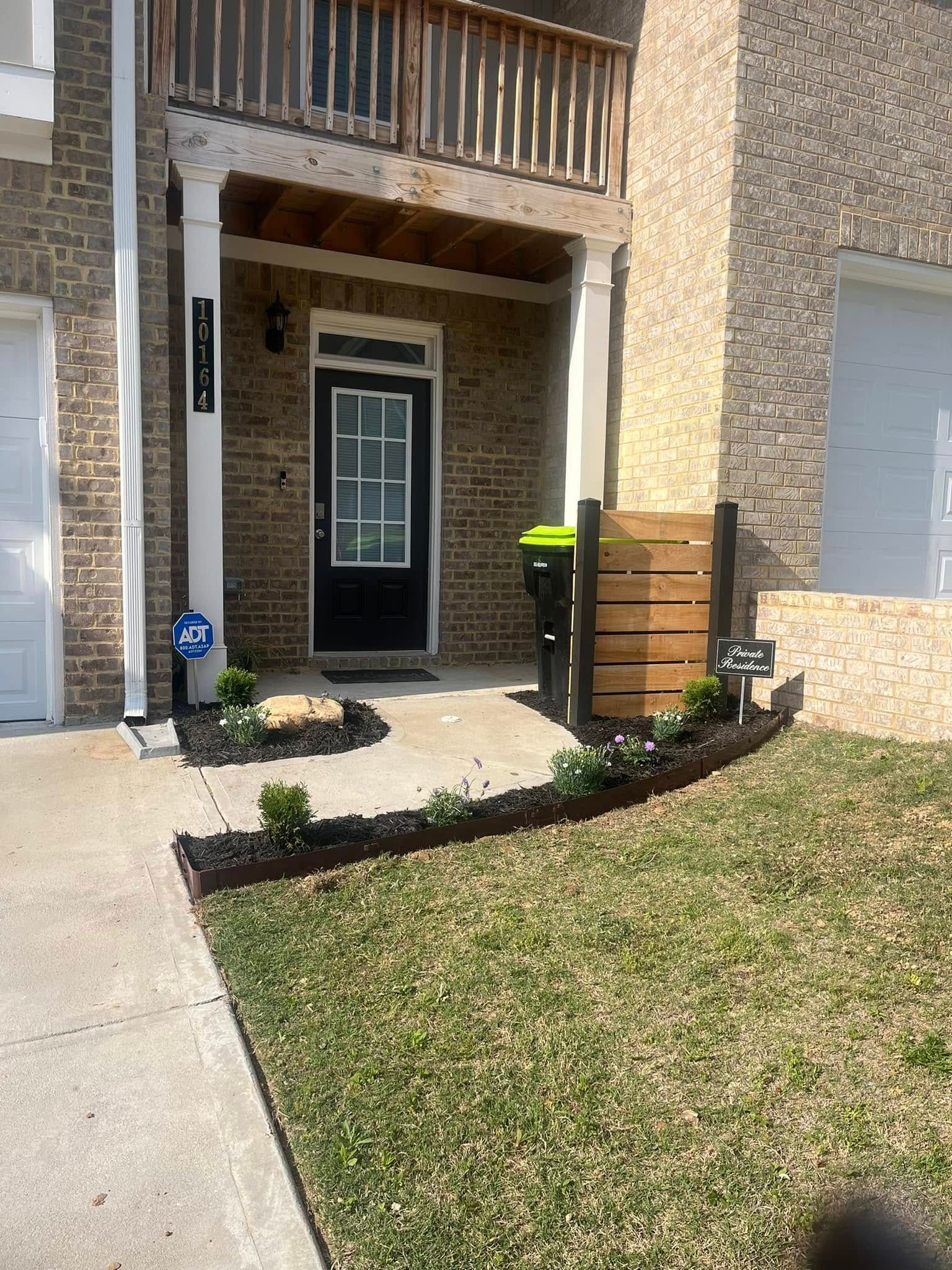 Exterior of a brick building with a black front door. Landscaping with mulch and plants in front.