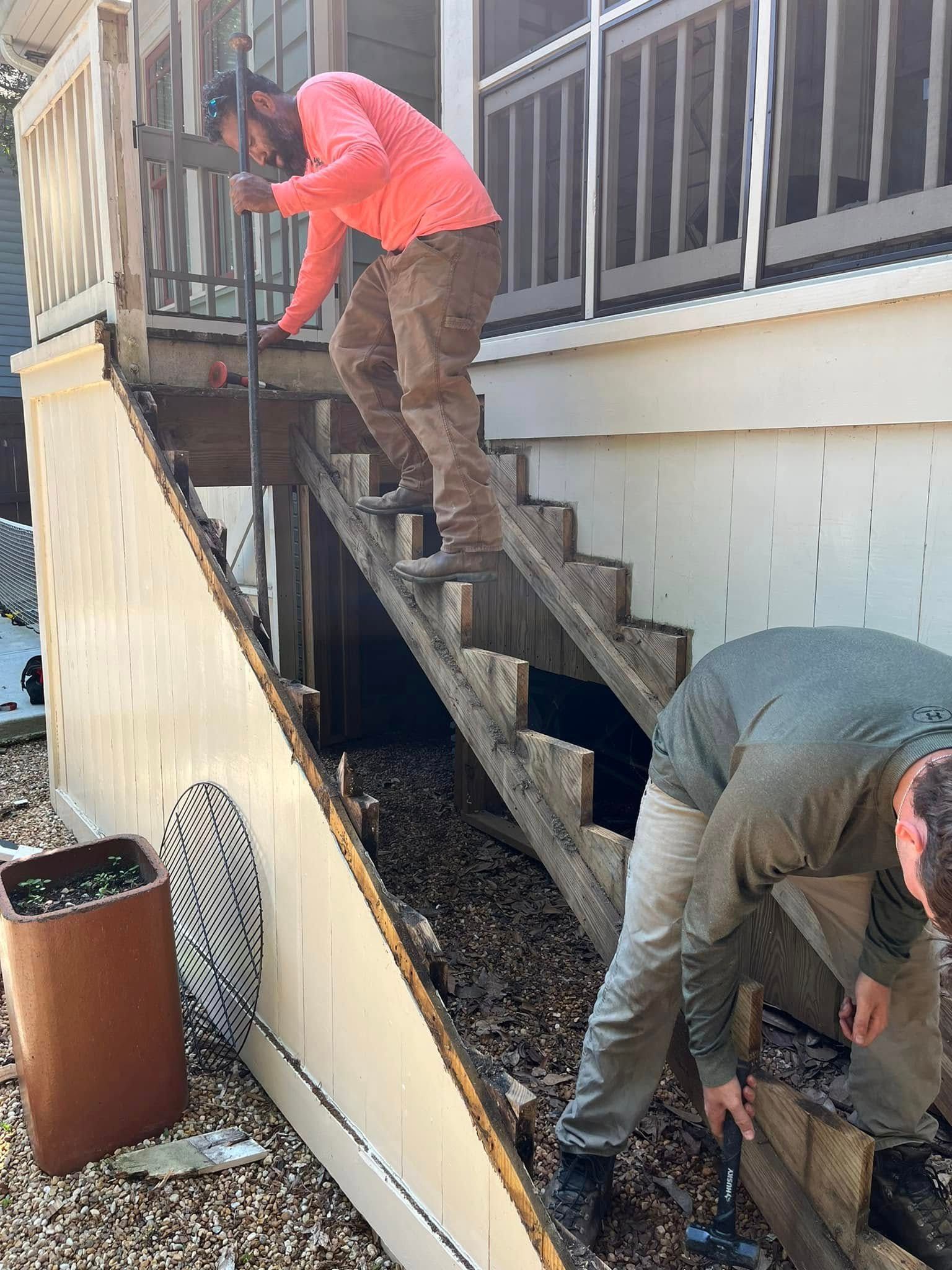 Two men repairing deteriorating outdoor stairs; one descends, other works at base.