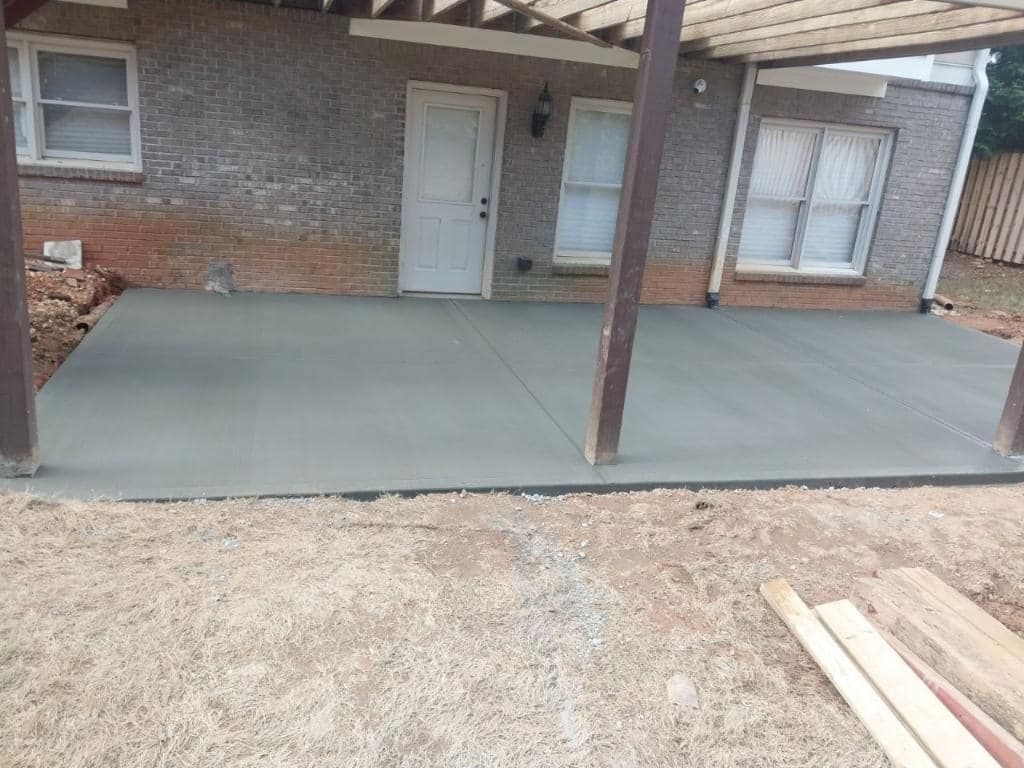 Newly poured concrete patio outside a brick building, under a pergola.