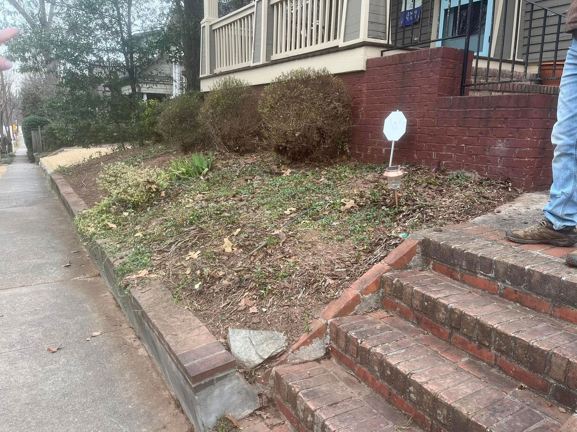 Brick steps lead up to a house with a small overgrown garden bed.