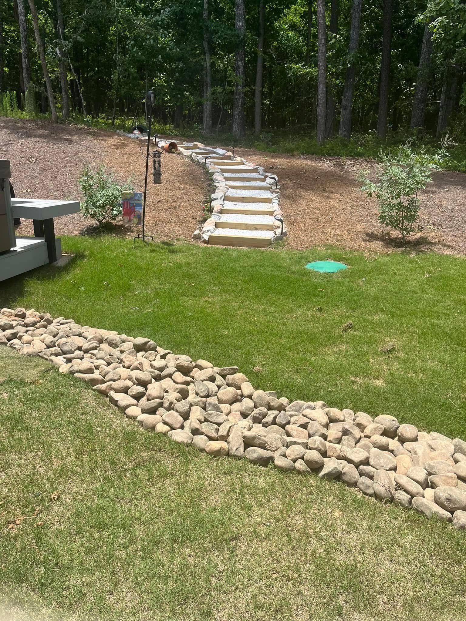 Stone steps leading up a hill through a wooded area; a rock border is in the foreground.
