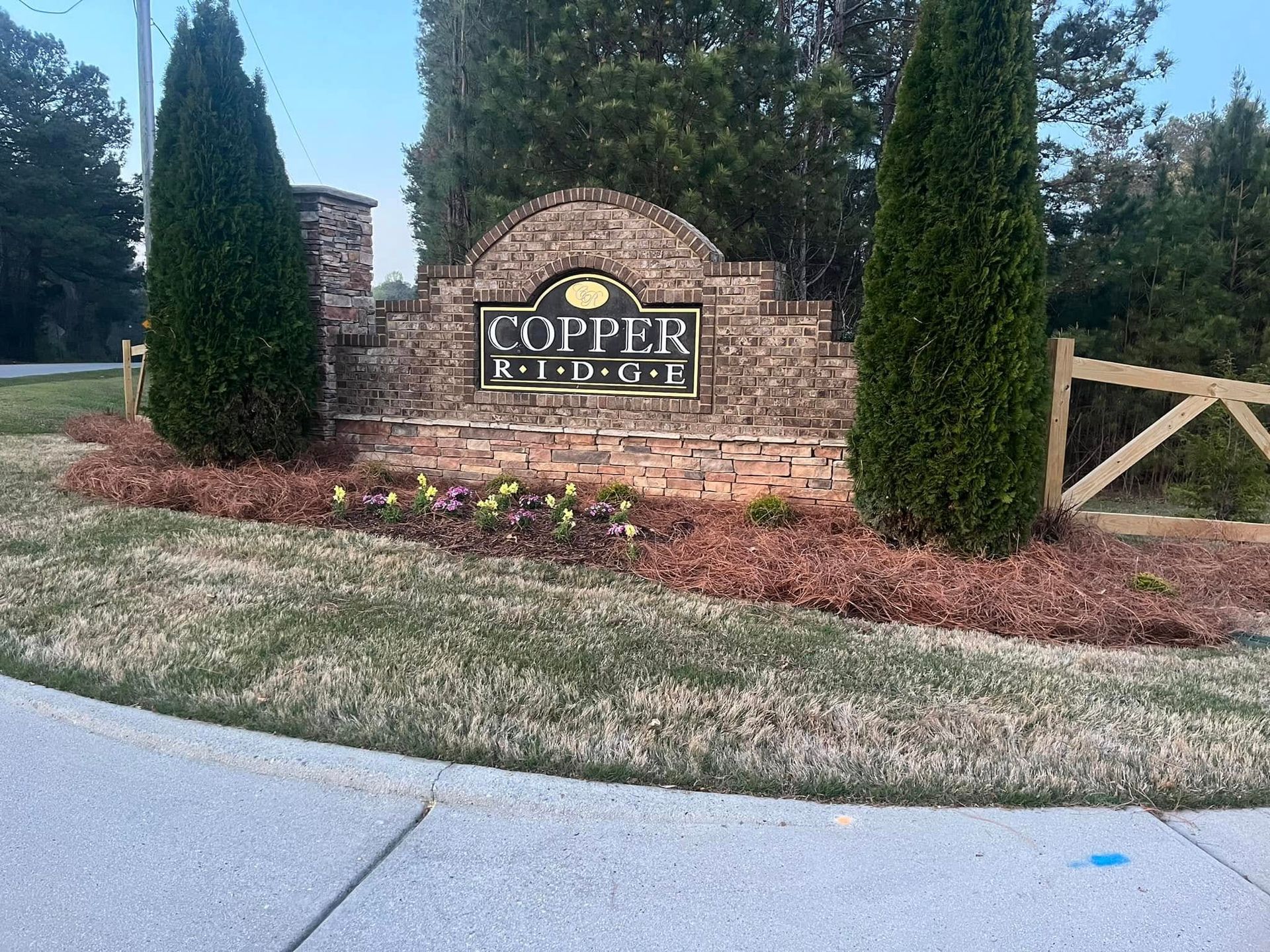 Entrance sign for Copper Ridge residential area, made of brick and stone. Flanked by green trees and flowerbed.