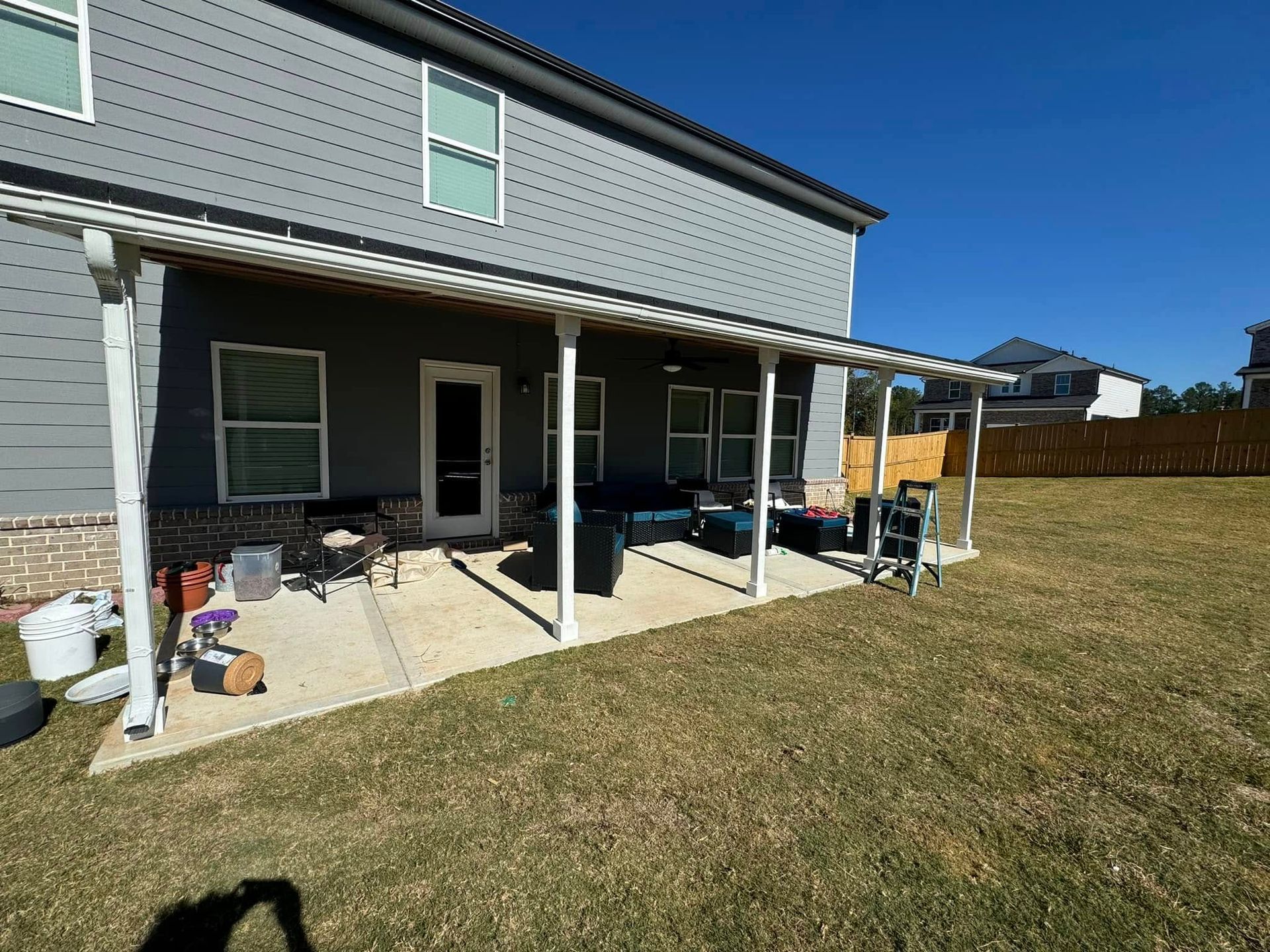 A white patio cover extends from a gray house. Backyard with grass and a clear blue sky.