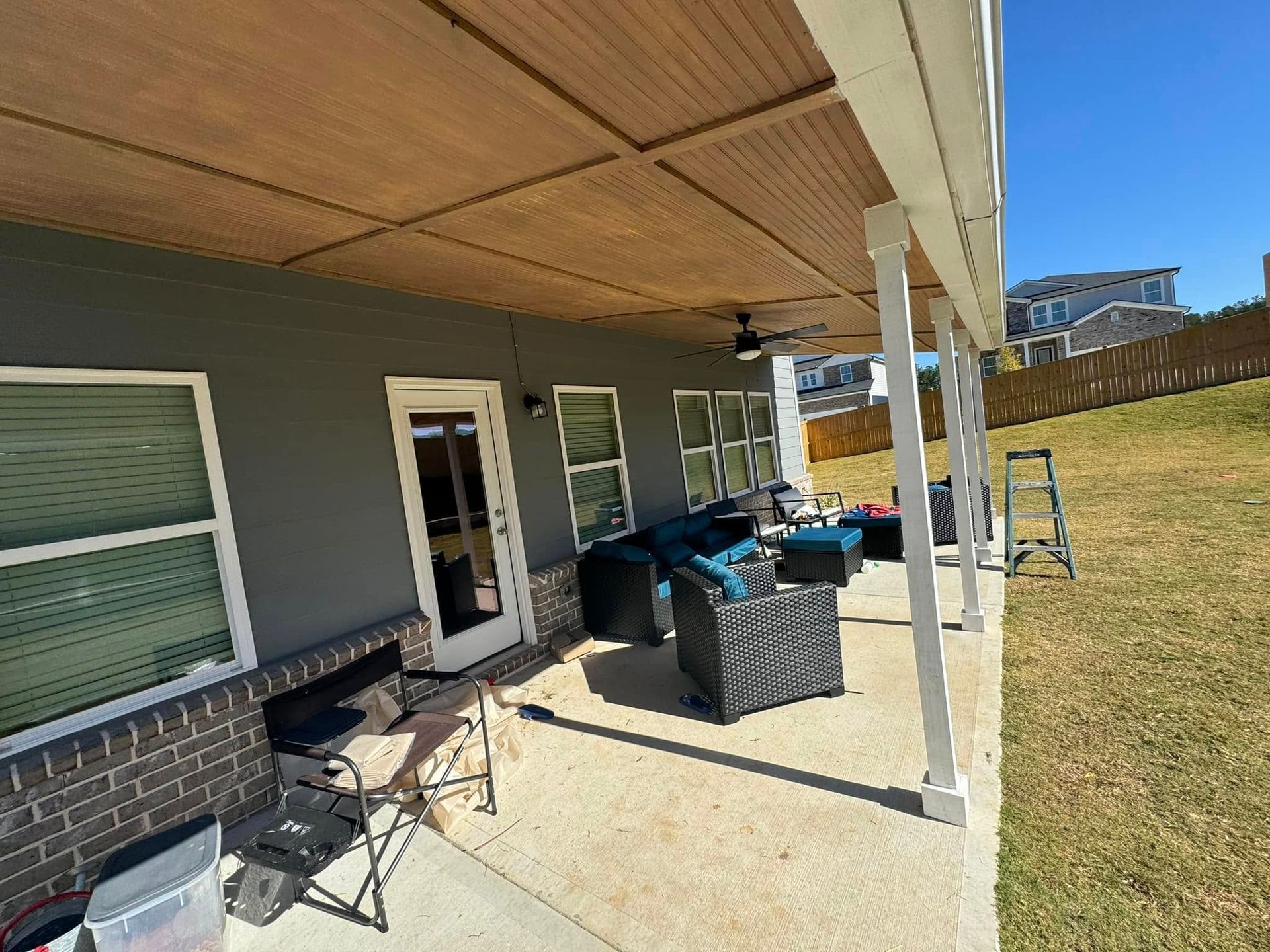 Backyard patio with furniture, gray wall, and brown overhead cover.