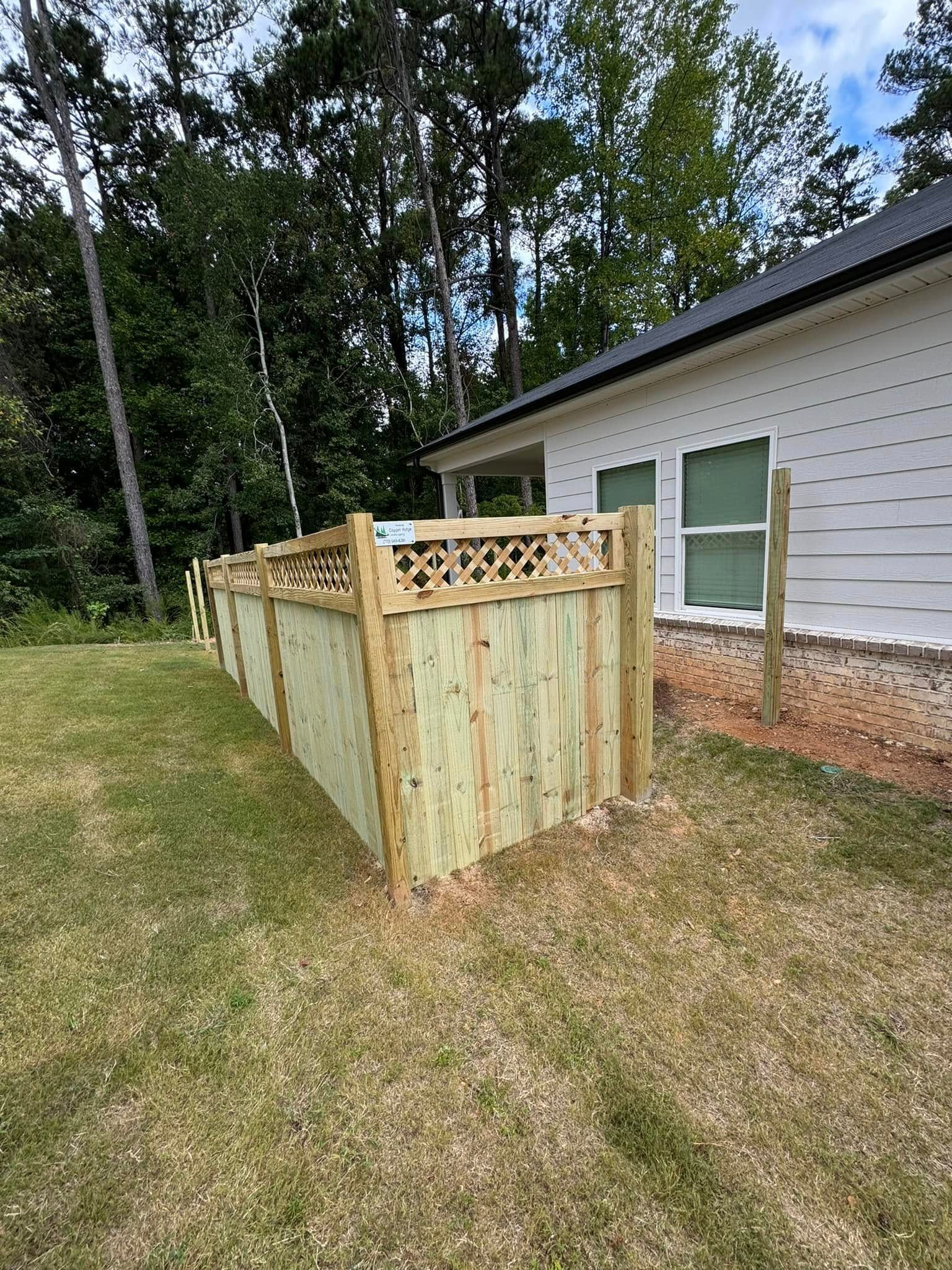 Wooden fence with lattice top along a white house and grassy lawn.