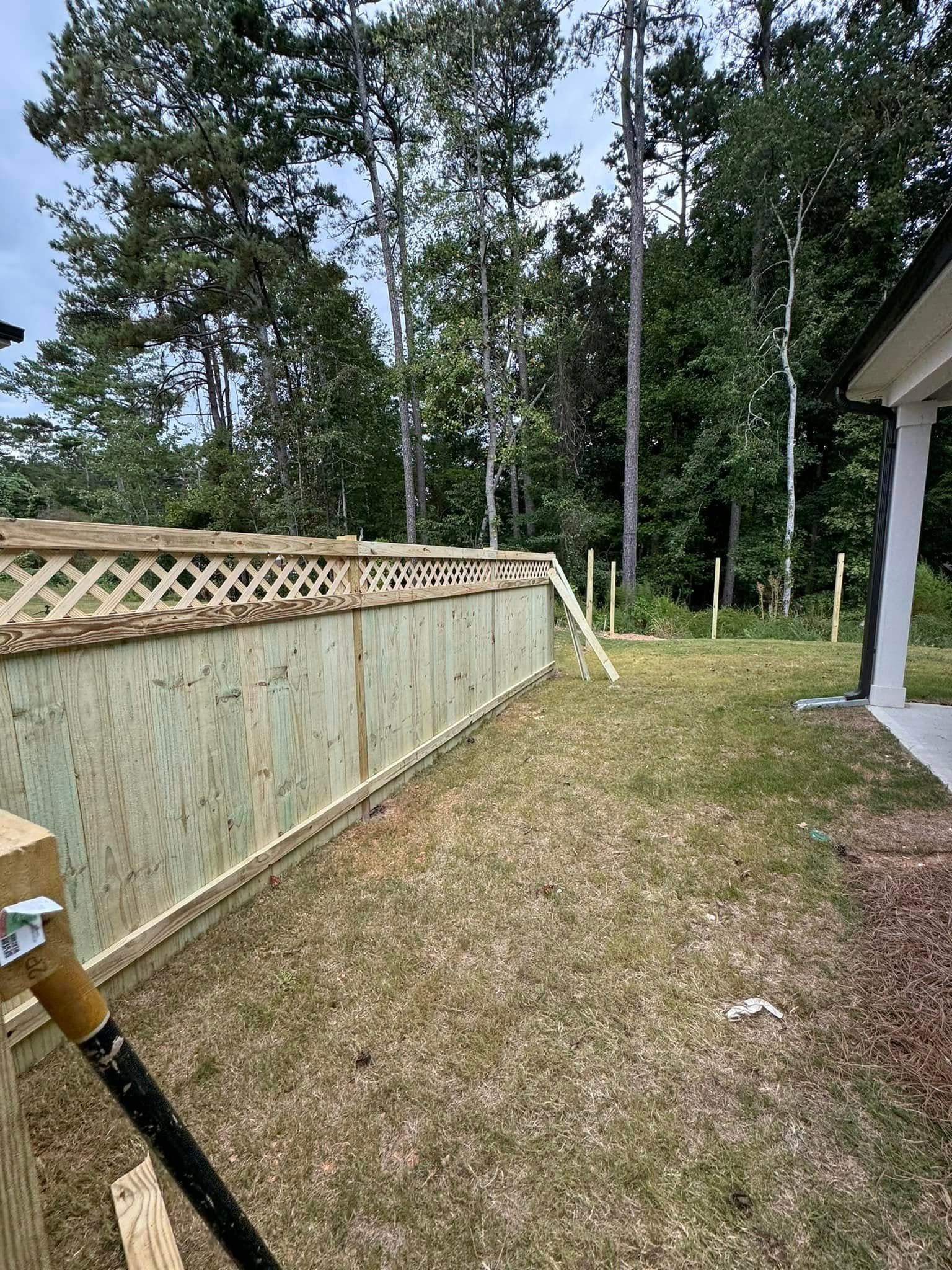 Wooden fence with lattice top, built in backyard, beside tall trees.