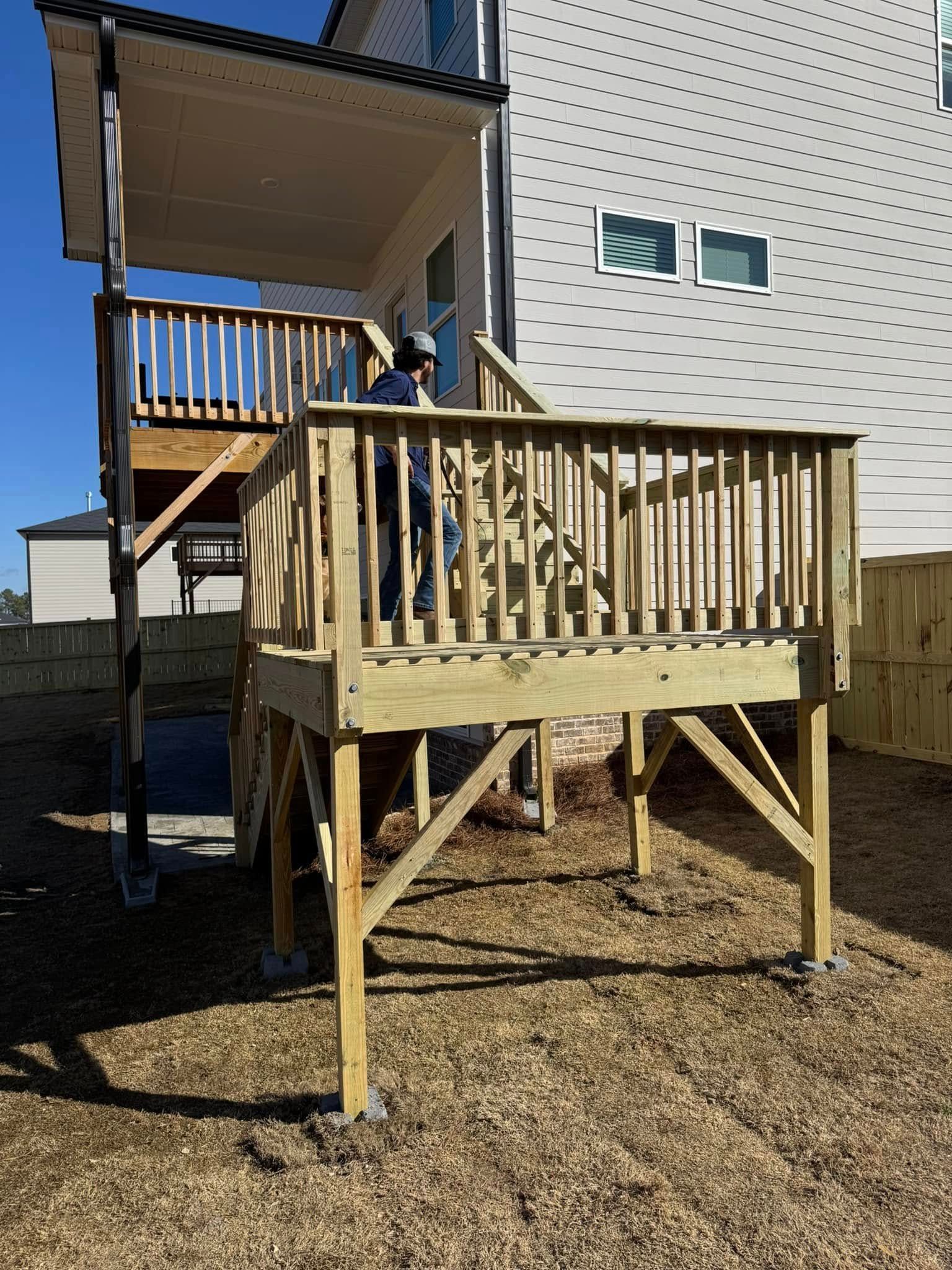Wooden deck attached to a house with a person standing on it, on a sunny day.