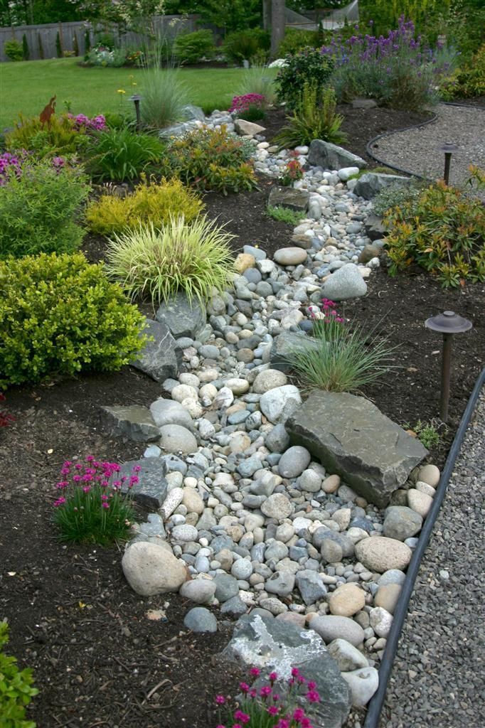 A rock garden with a dry creek bed winding through it, surrounded by colorful plants and shrubs.