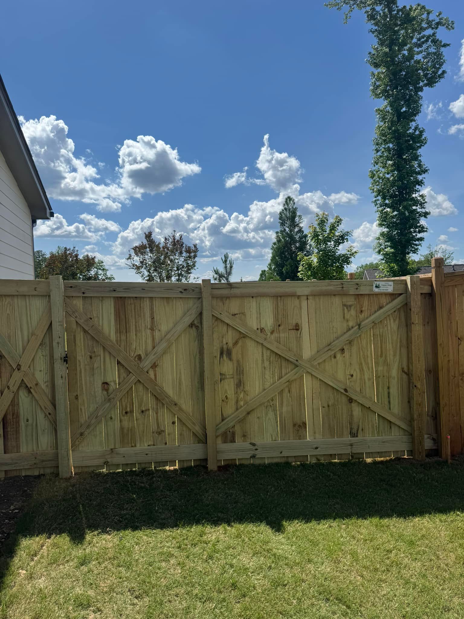 Wooden gate in a backyard on a sunny day. Blue sky with white puffy clouds overhead. Green grass.