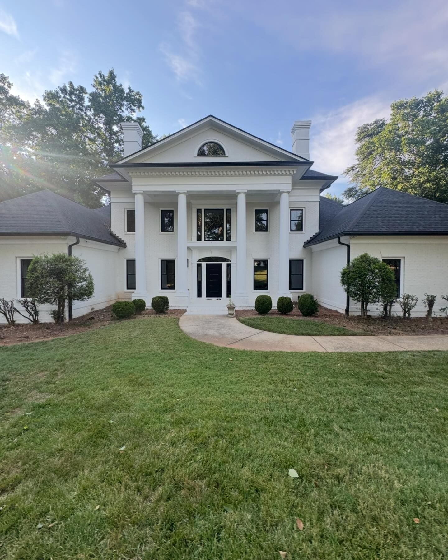 White house with large columns, black roof, and manicured lawn under a partly cloudy sky.