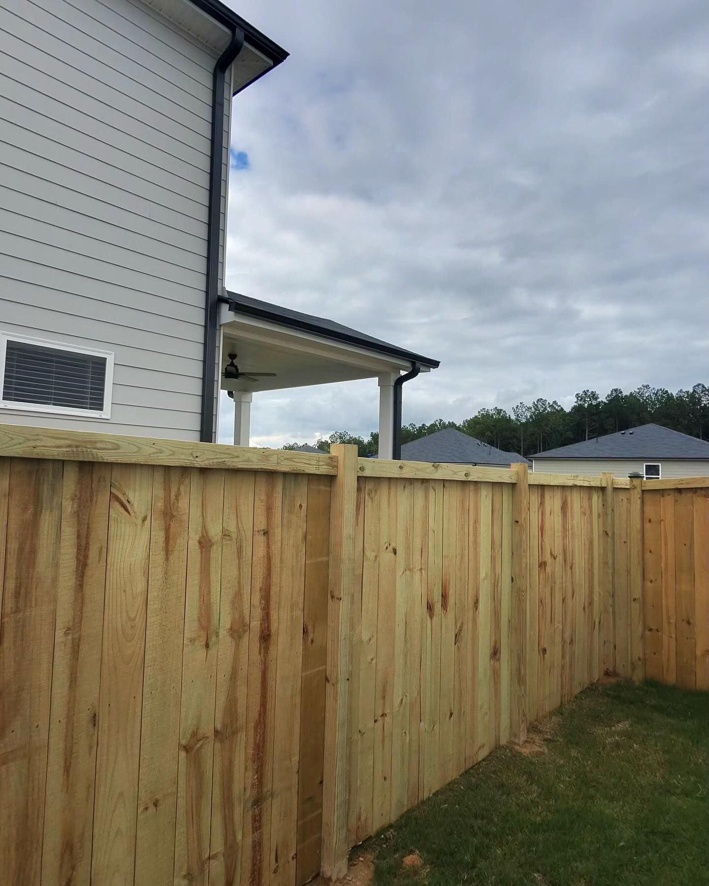 Wooden fence in front of a light gray house under a cloudy sky.
