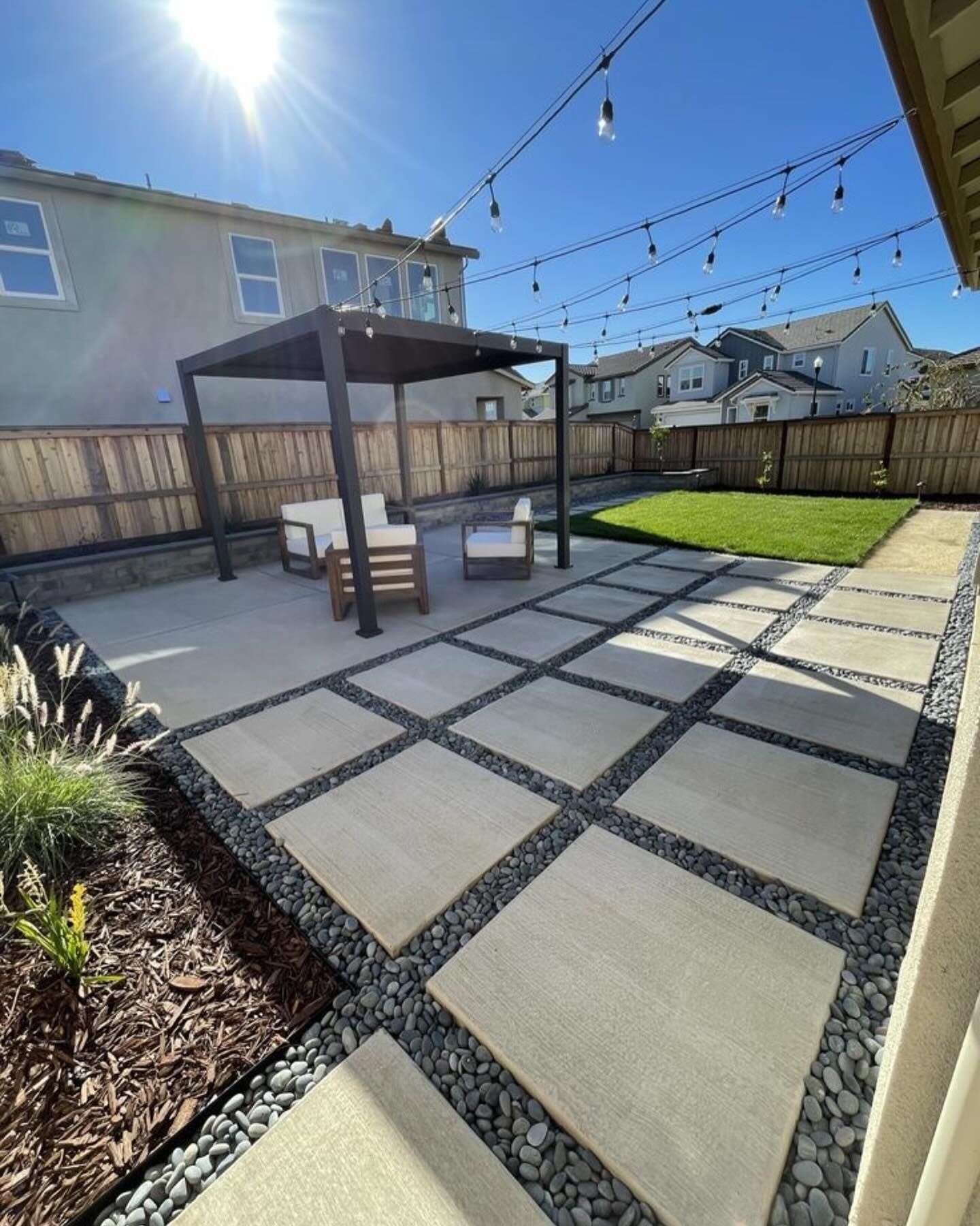 Backyard patio with concrete pavers, gravel, pergola, seating, and string lights.