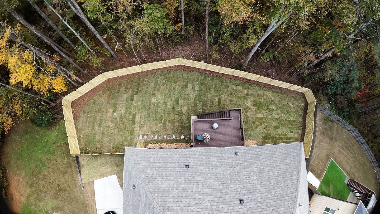 Aerial view of a house with a gray roof and a backyard with a retaining wall and trees.