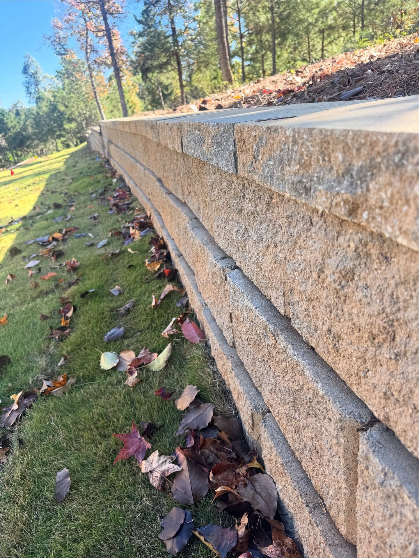 Stone retaining wall on a grassy hillside, scattered with fallen leaves.