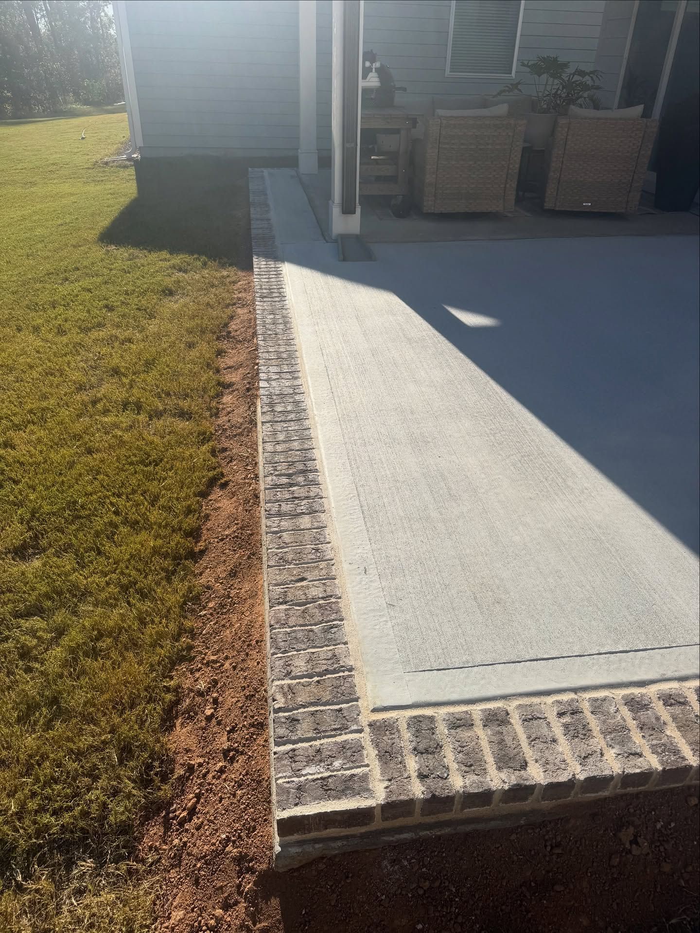 Concrete patio with brick border next to lawn and building.