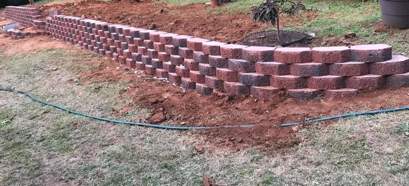 Brick retaining wall in a yard, built with dark red interlocking bricks.
