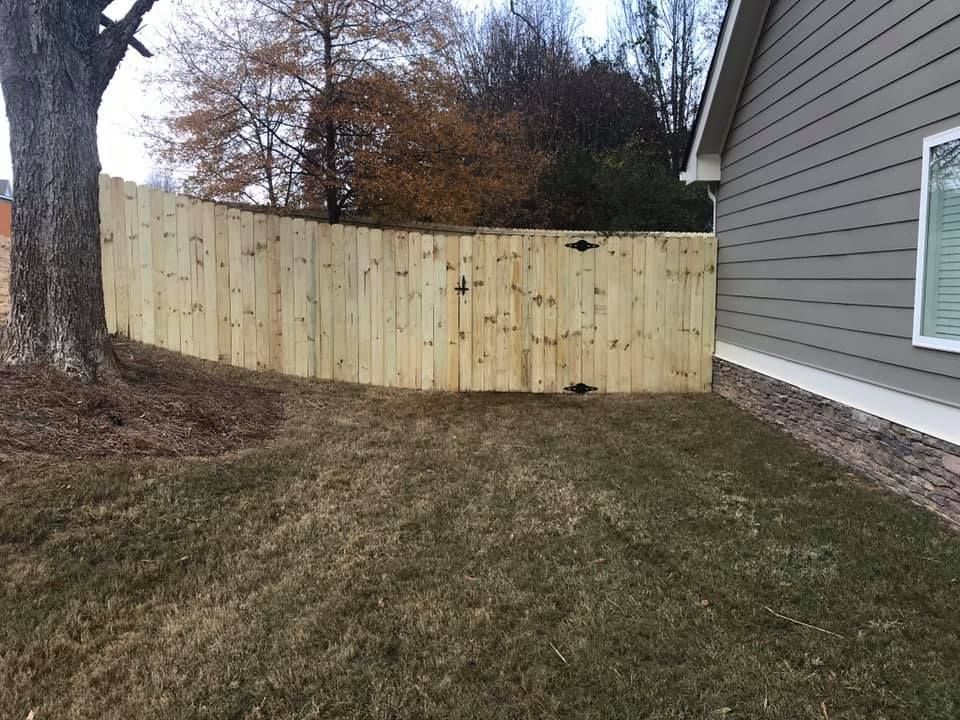 Wooden fence surrounding a yard, with a gate and a house on the right.