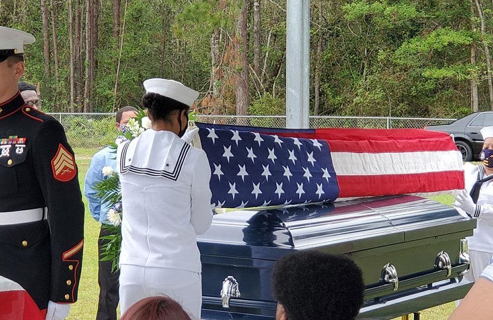 A woman is holding an american flag and a rose at a funeral.