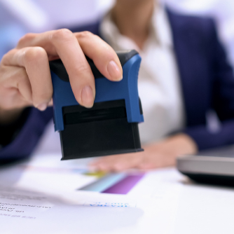 Person in a blue suit stamps a document with a black and blue stamp on a desk.
