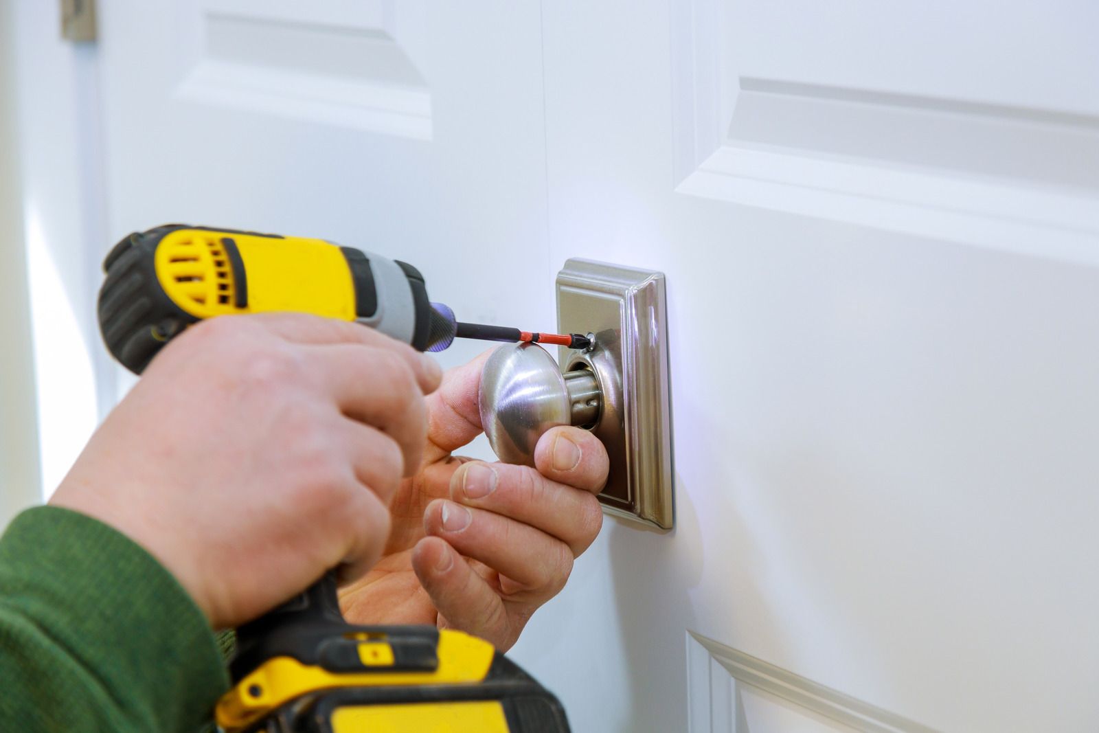 Person using a yellow drill to install a silver doorknob on a white door.