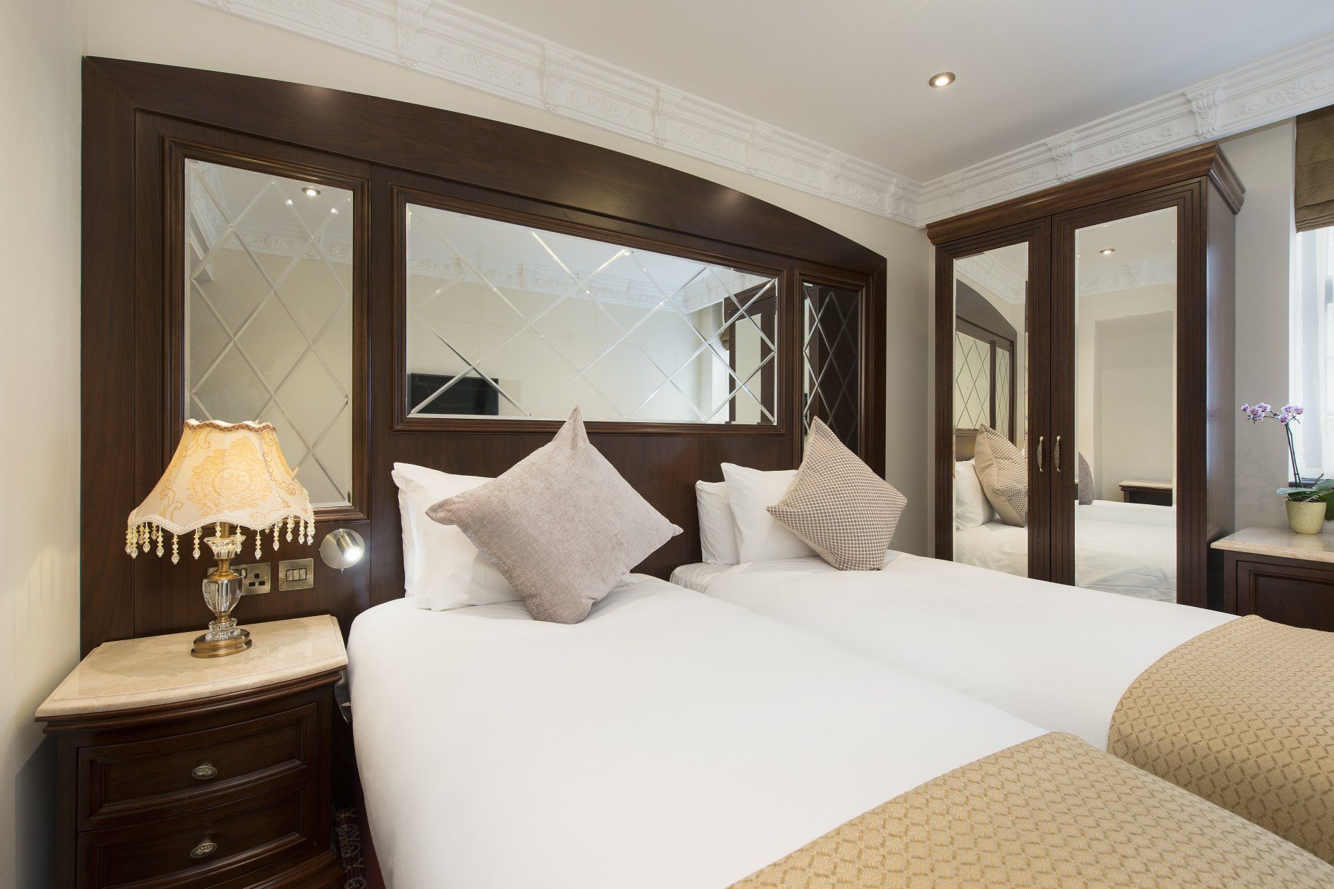 Twin hotel beds with pillows, nightstands, a lamp, and a large mirror headboard.
