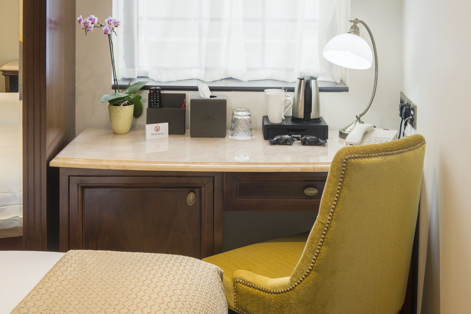 Desk with yellow chair, lamp, and coffee station in front of a window.