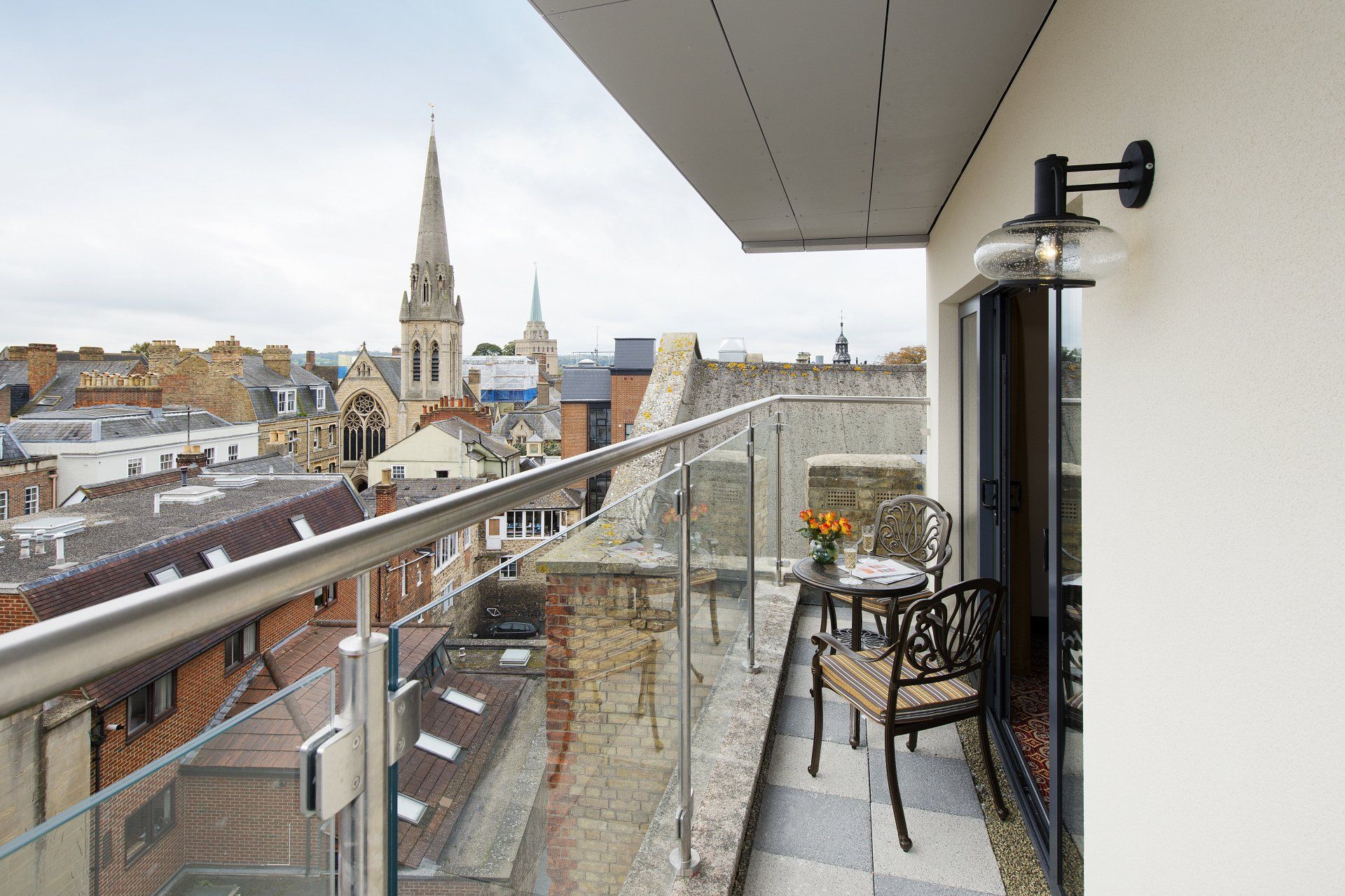 Rooftop balcony with a table and chairs, overlooking a cityscape with church steeples.
