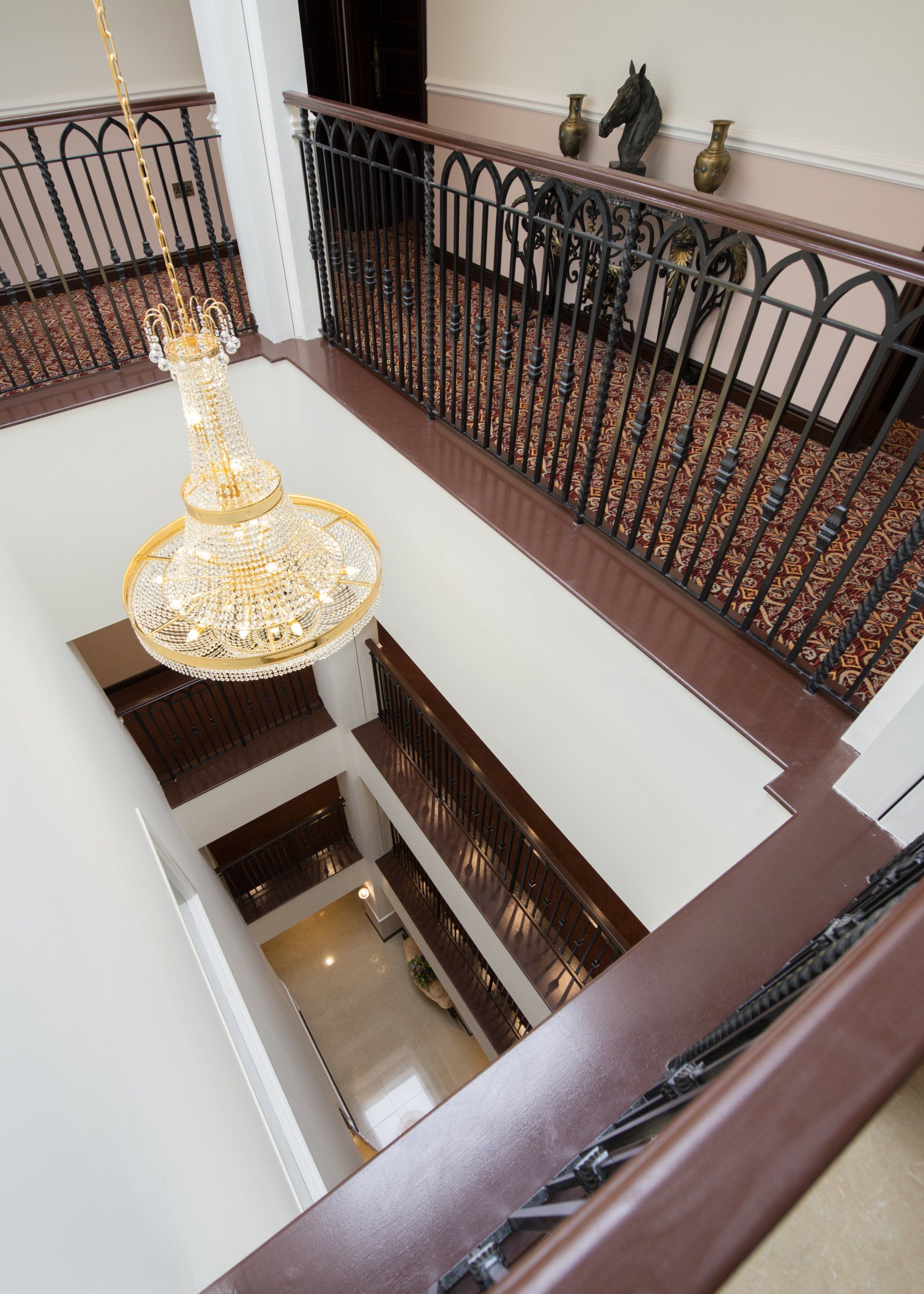 High-angle view of a multi-story foyer with a chandelier, dark railings, and ornate detailing.