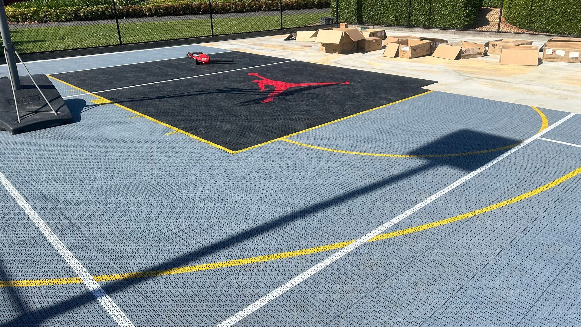 Basketball court with black and red Jordan logo, surrounded by gray and blue flooring, net and lines.