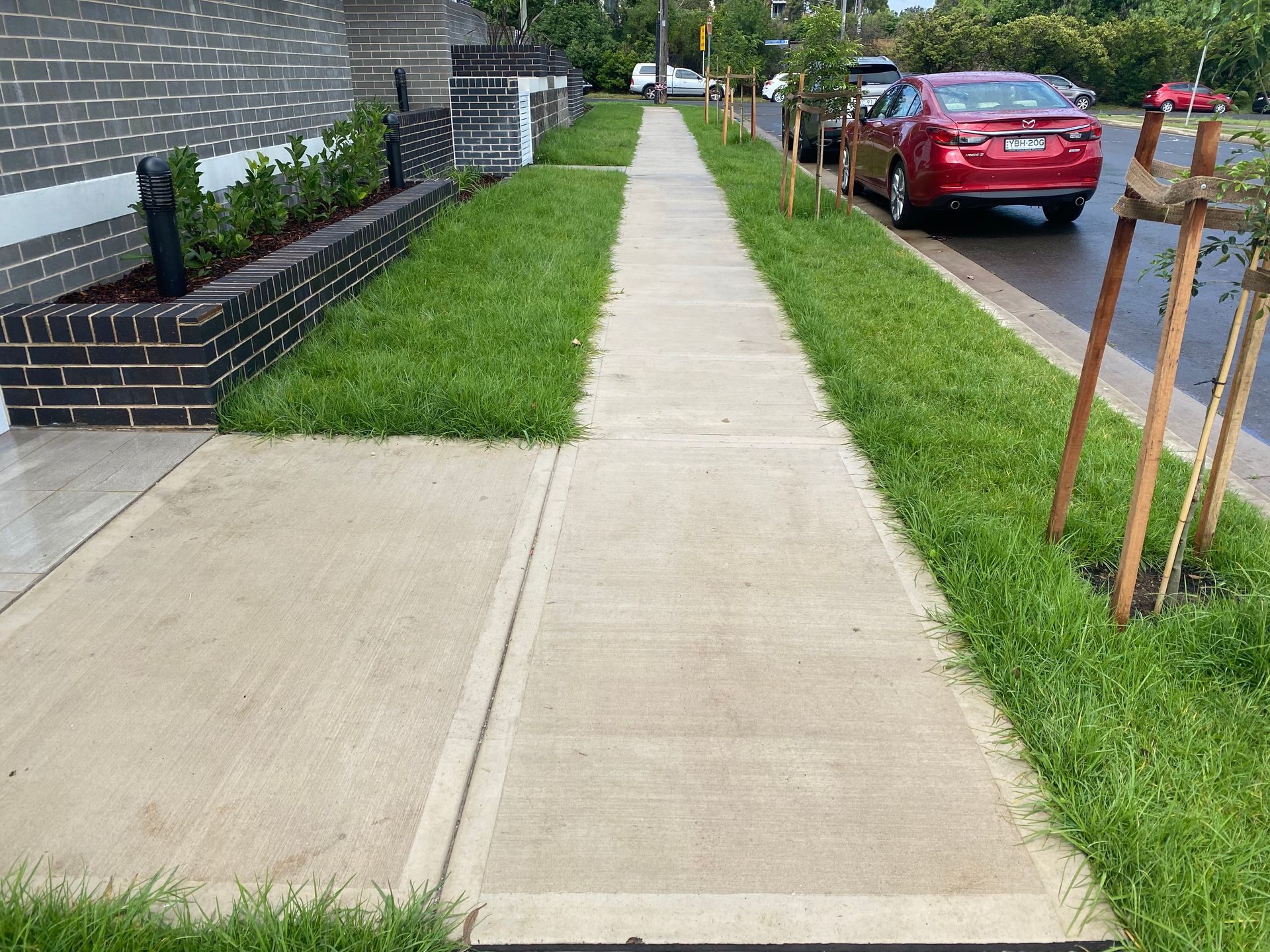 Concrete sidewalk with green grass borders; red car parked on right.