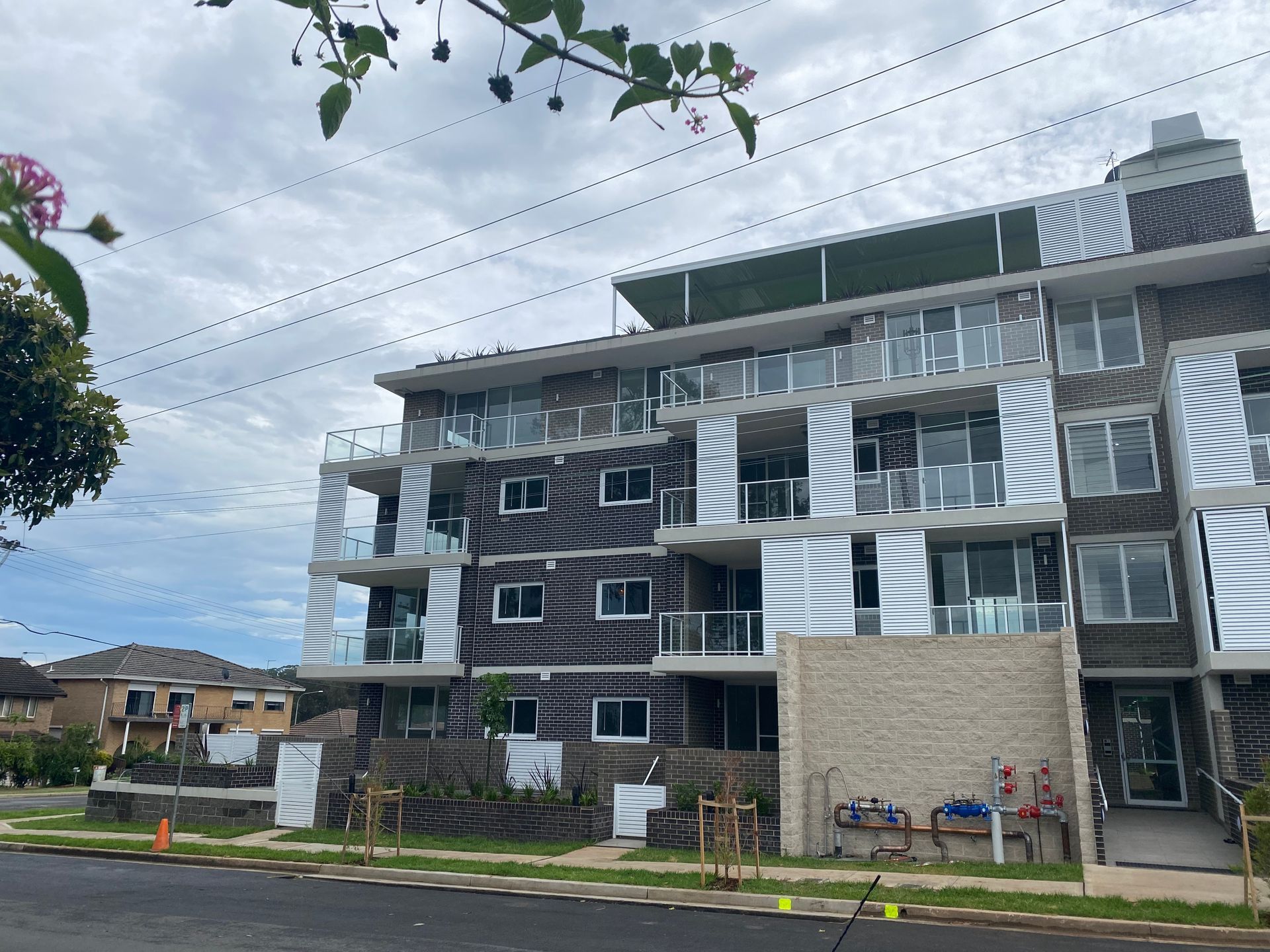 Modern multi-story apartment building with balconies, brick exterior, and power lines overhead.