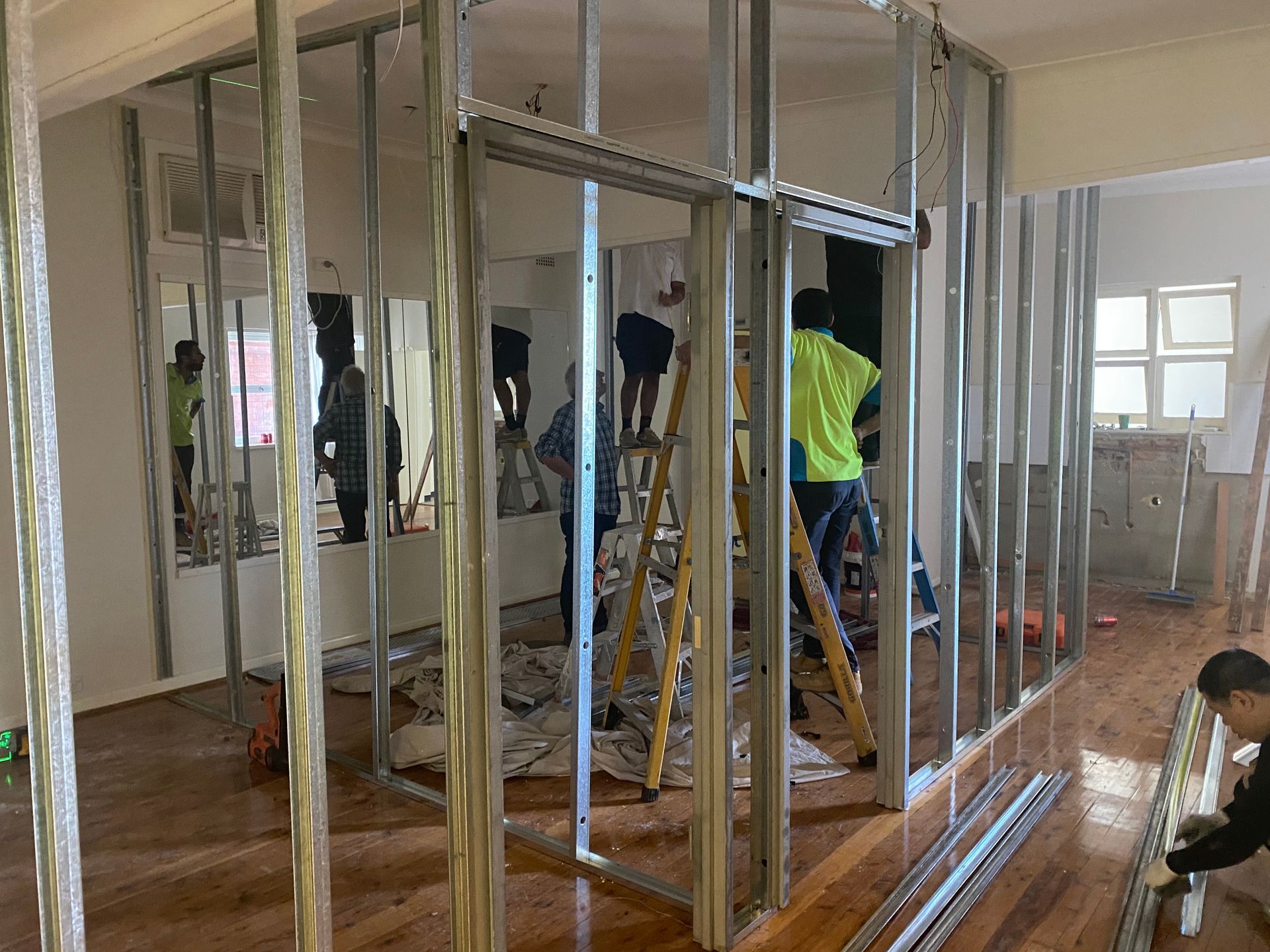 Construction workers installing metal stud framing for a new interior wall, interior setting.