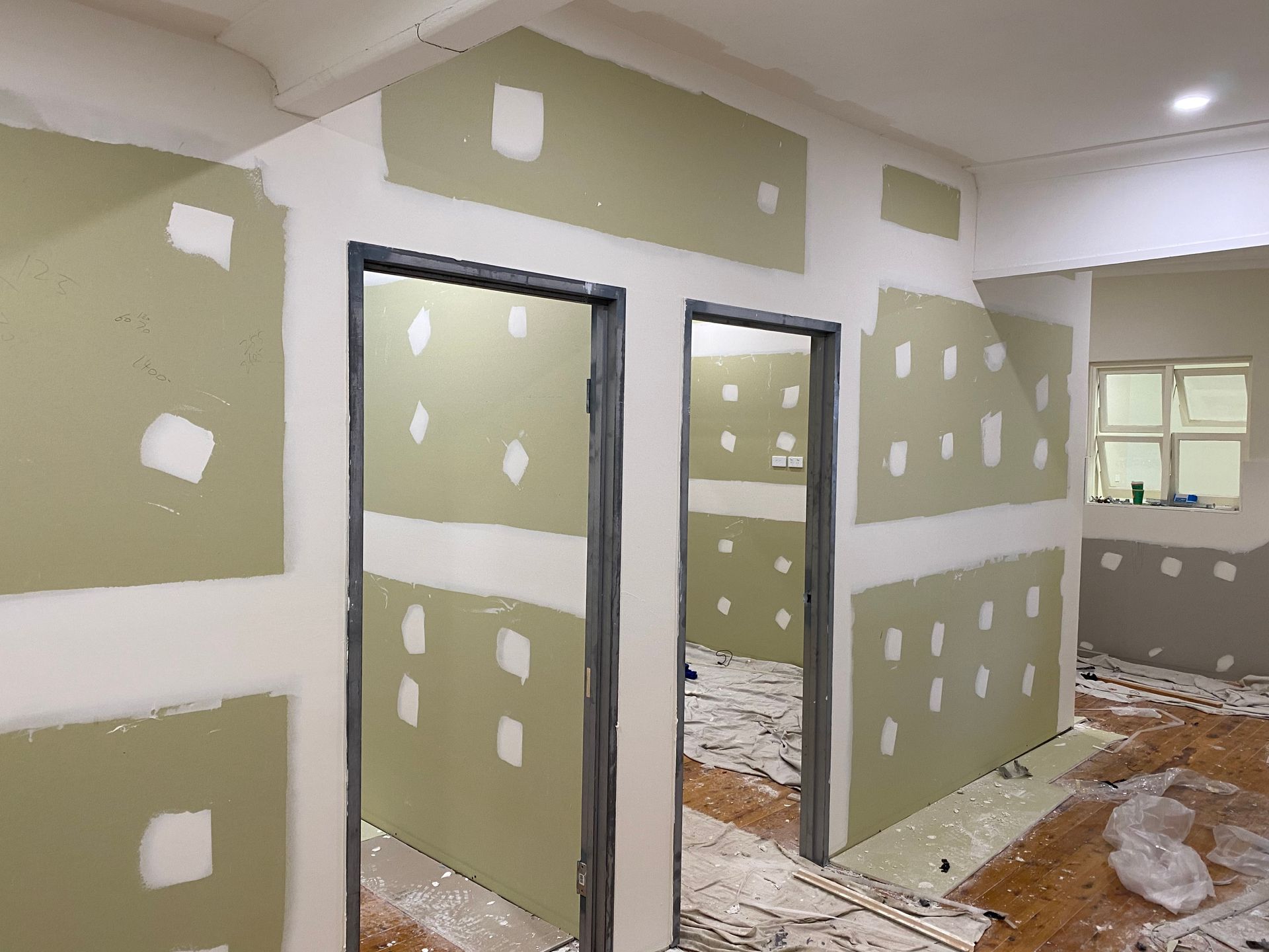 Interior room under construction, with drywall partially installed. Doors, beige walls, and white joint compound visible.