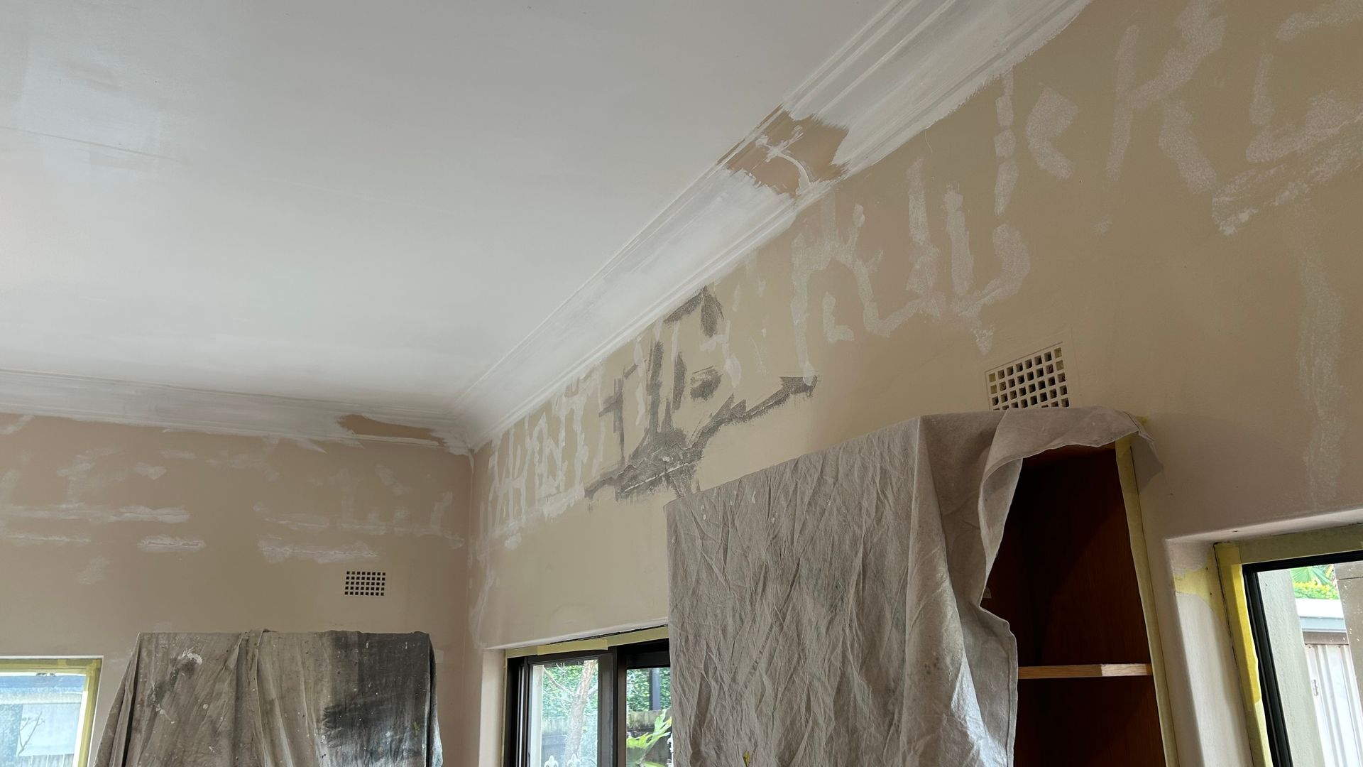 Interior wall with peeling paint and covering. Ceiling with crown molding.
