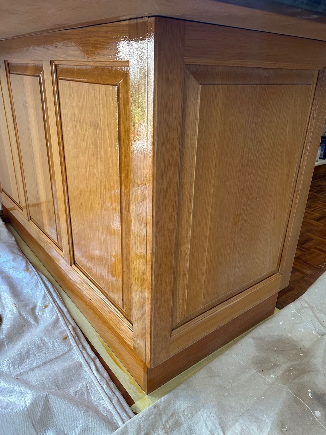Wooden cabinet corner, stained, varnished, with light reflecting off the surface.