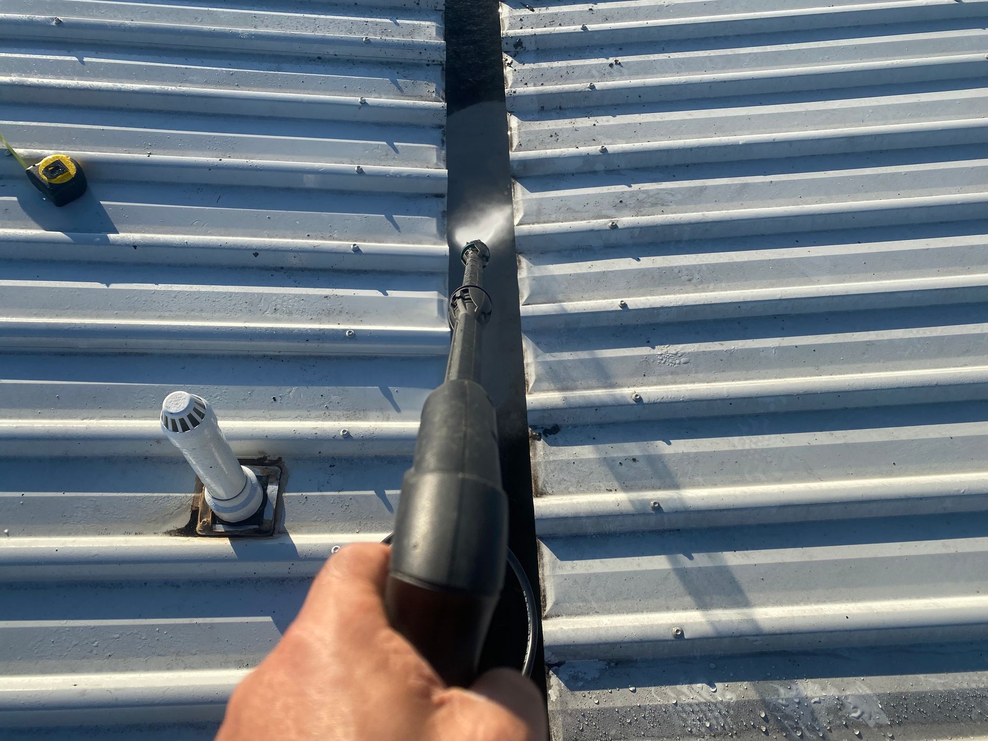 Person sealing a seam on a corrugated metal roof with a caulking gun. High pressure water cleaning.