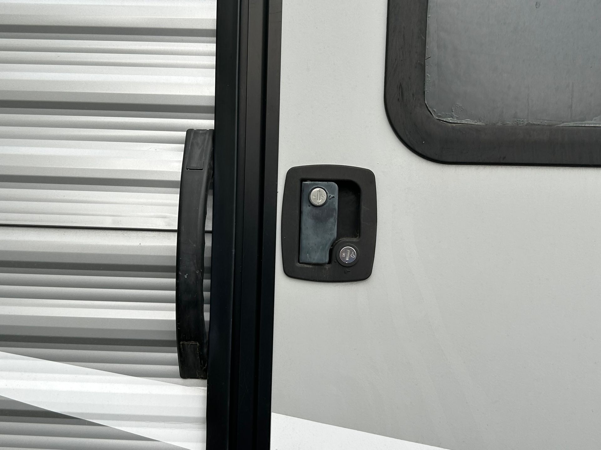 RV door with black handle and lock on a gray and white exterior.