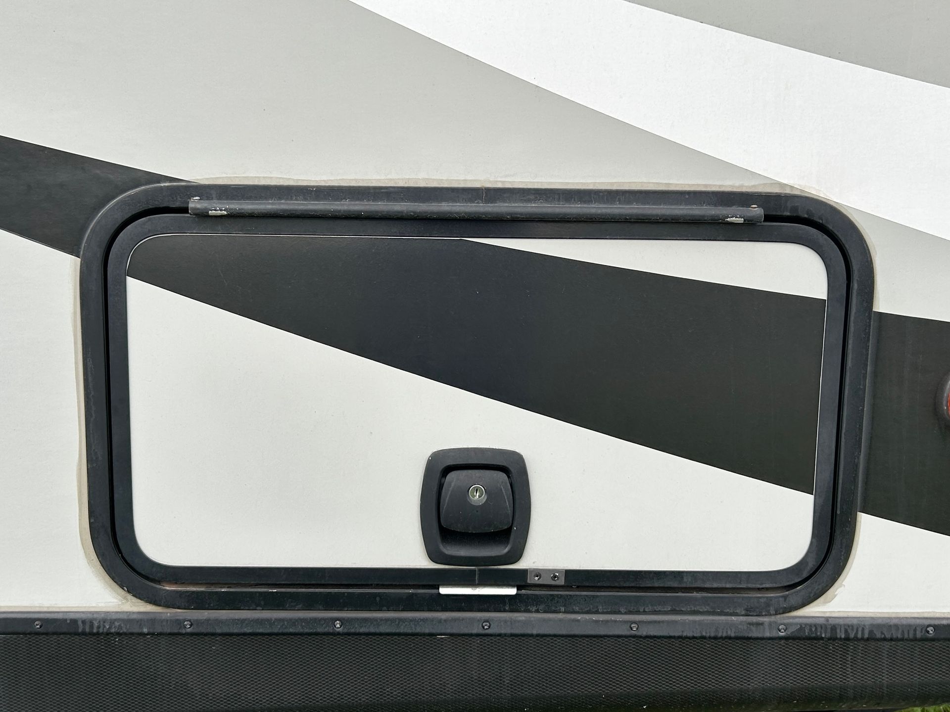 RV storage compartment with black frame and latch on a white and black exterior.