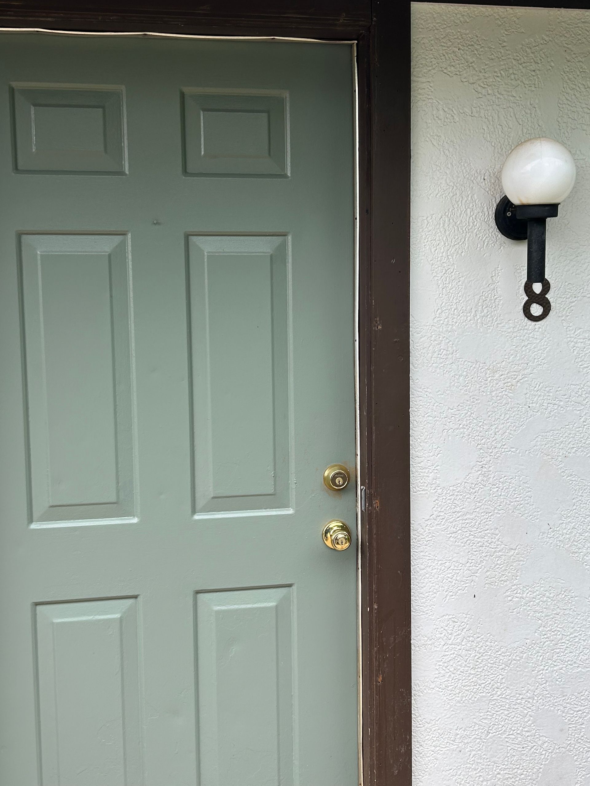 Green door with gold hardware next to white stucco wall with black lamp.