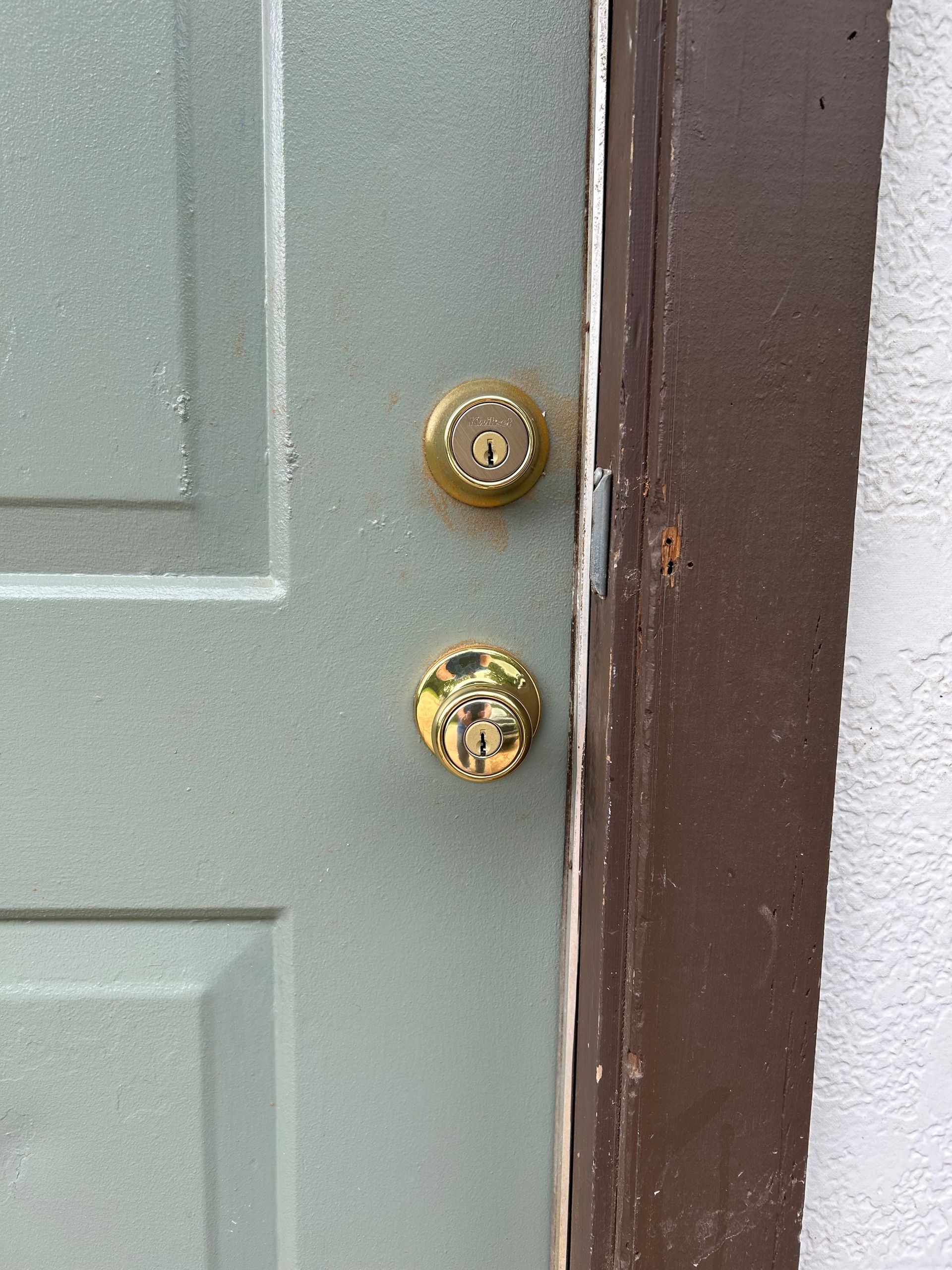Green door with gold doorknob and lock, brown trim.