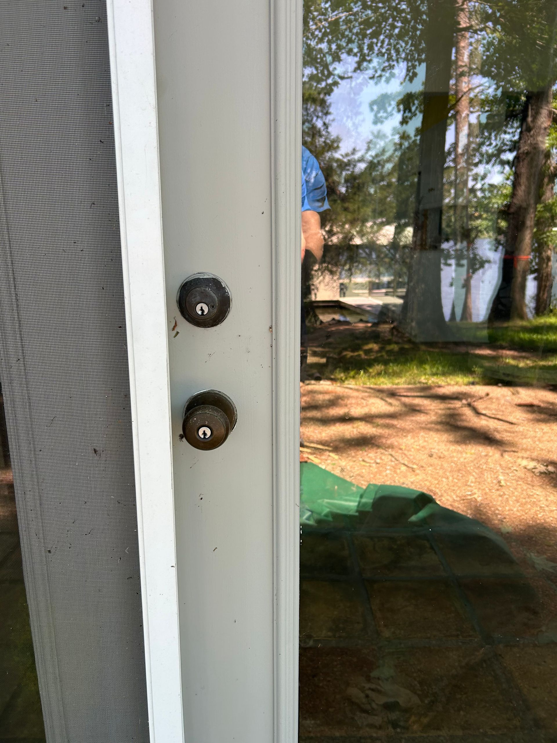 White door frame with two dark metal knobs. Reflective glass shows outdoor trees and foliage.