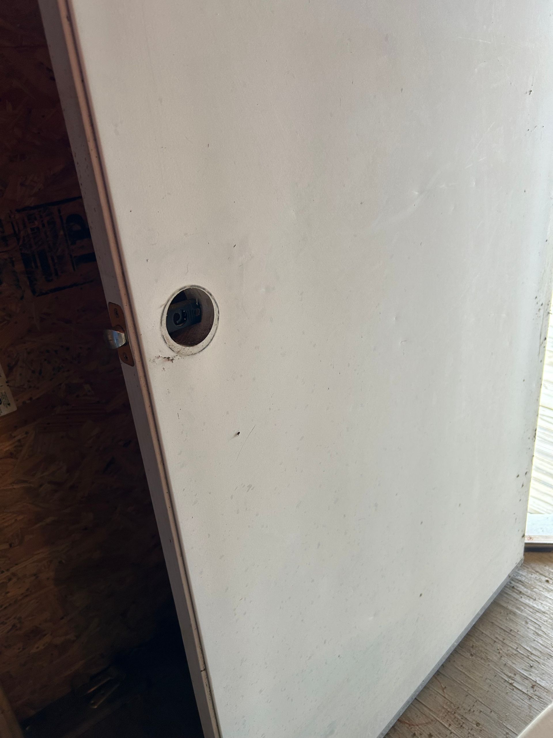 White door with a hole for a doorknob, set in a wooden frame.