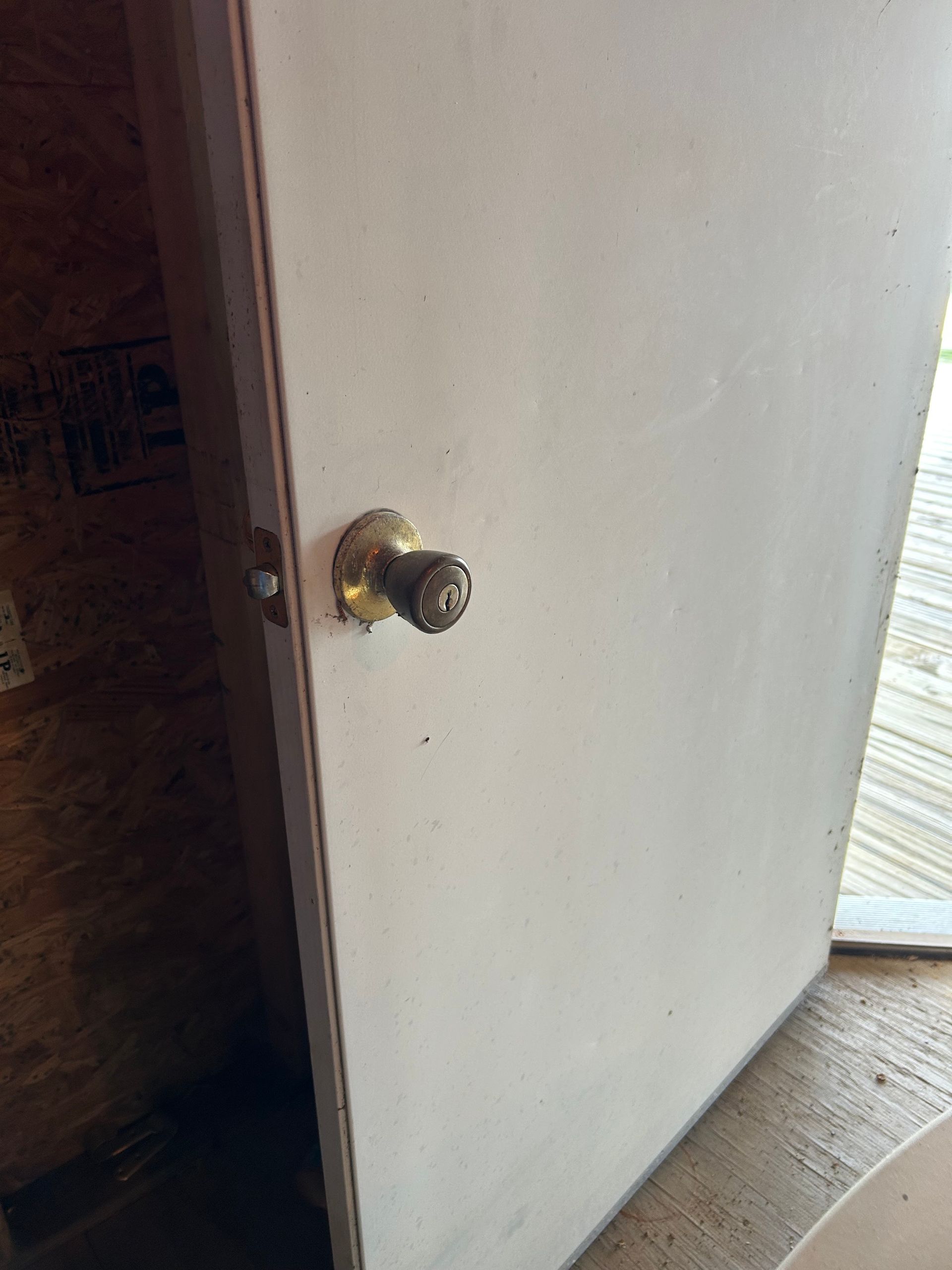 White door with tarnished brass doorknob slightly ajar, set in a wooden frame.
