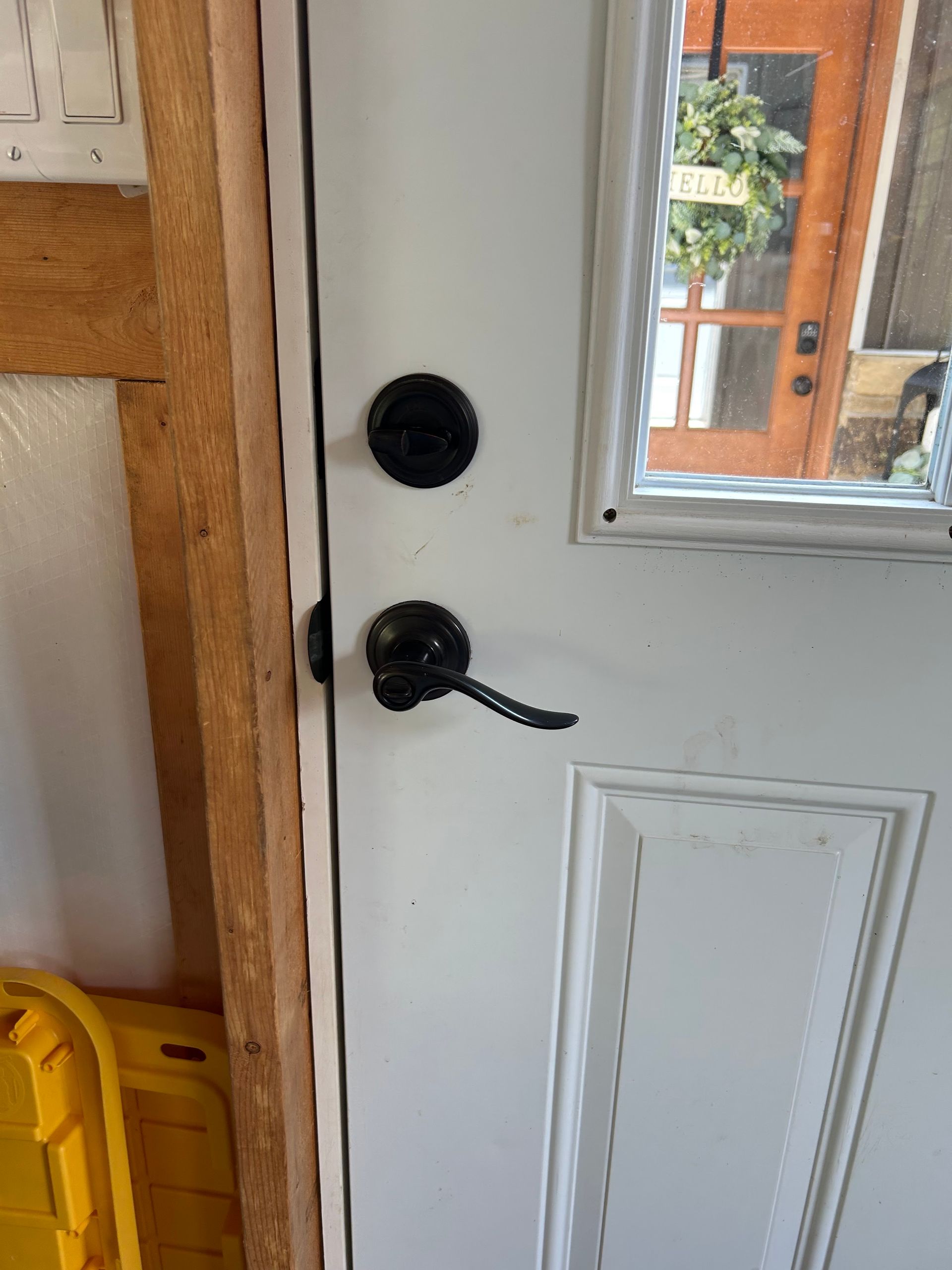 White door with black handle and deadbolt. Window reveals a wreath on another door.