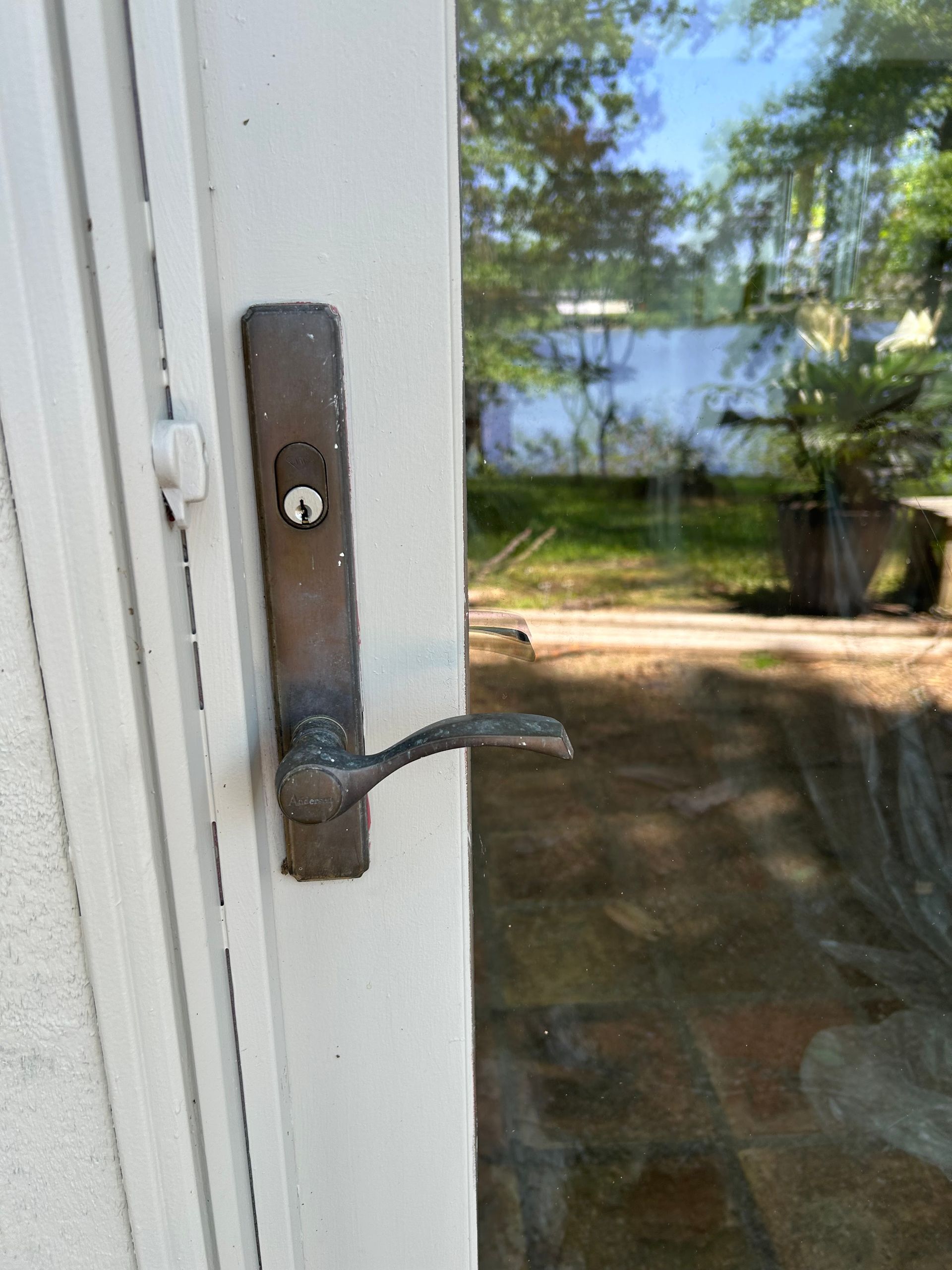 Bronze door handle and lock on a white door. Outdoor view through the glass.