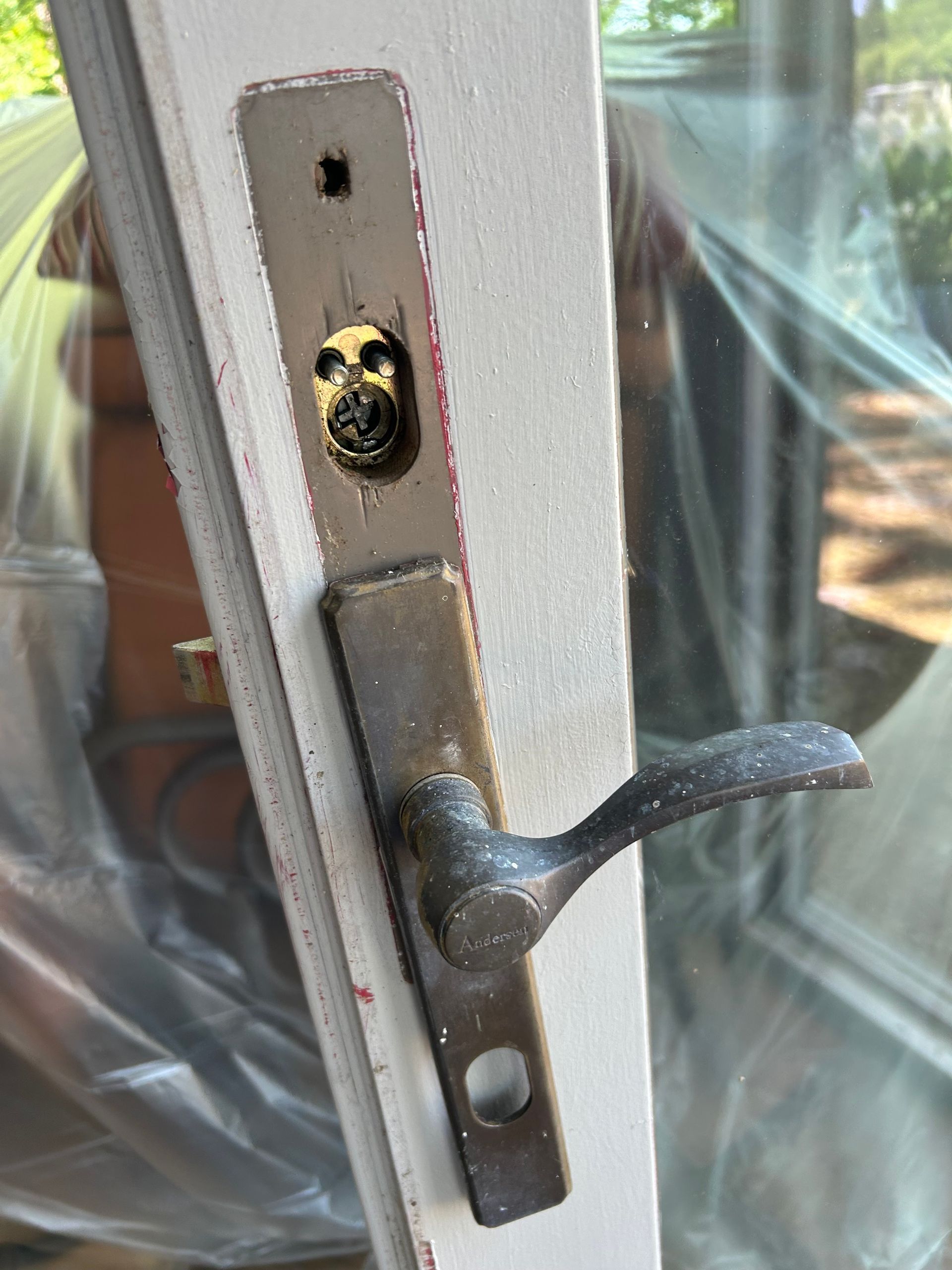 Close-up of a door handle and lock plate on a white door. The hardware is aged, with wear and tear visible.