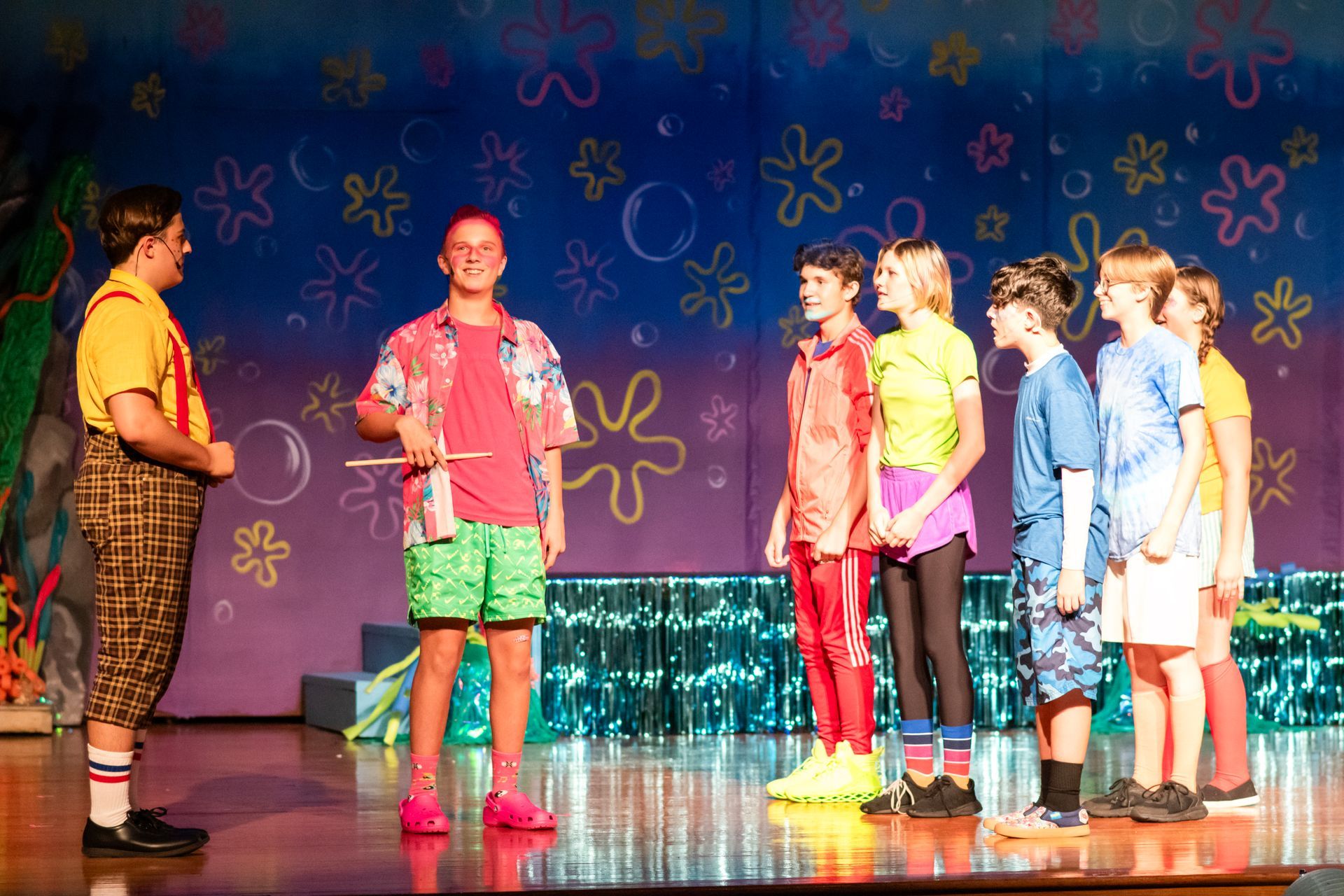 A stage production: Young actors in colorful costumes on a stage with a sea-themed backdrop.