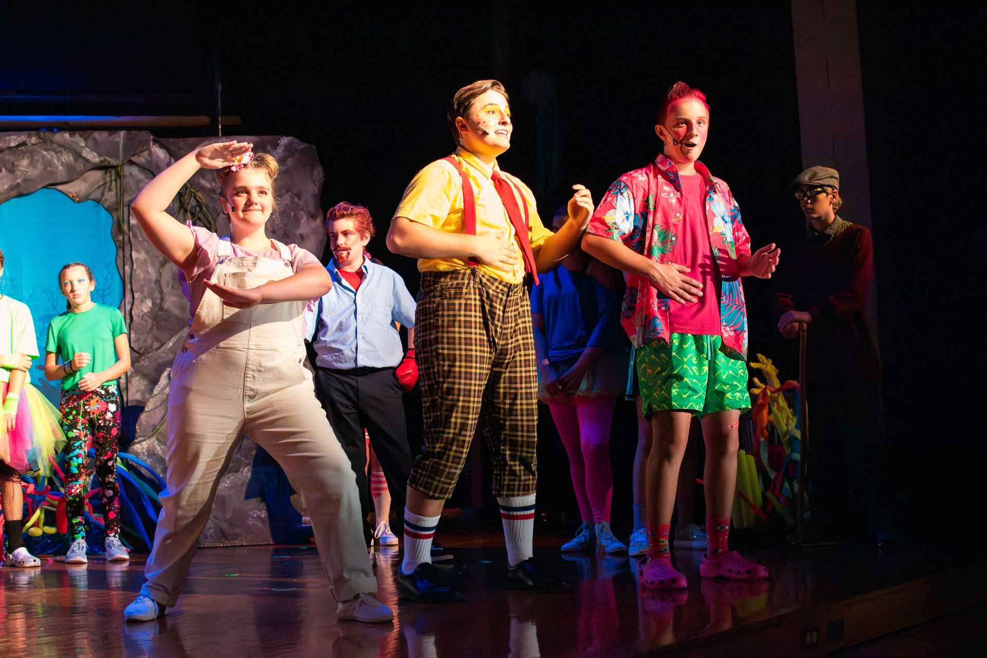 Group of young people in colorful costumes performing a play on stage.