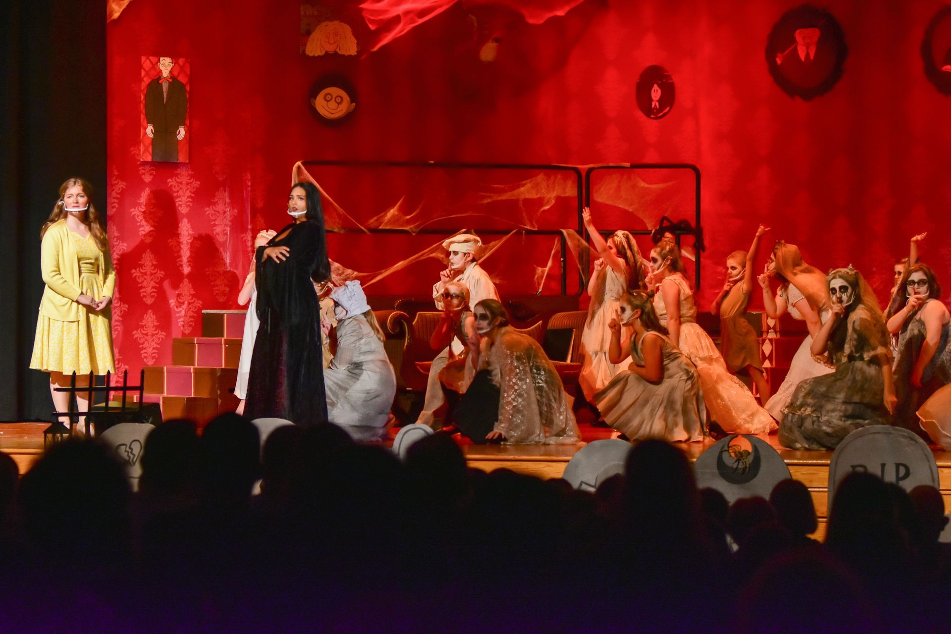 Stage production with performers in costume, red backdrop, audience watching.