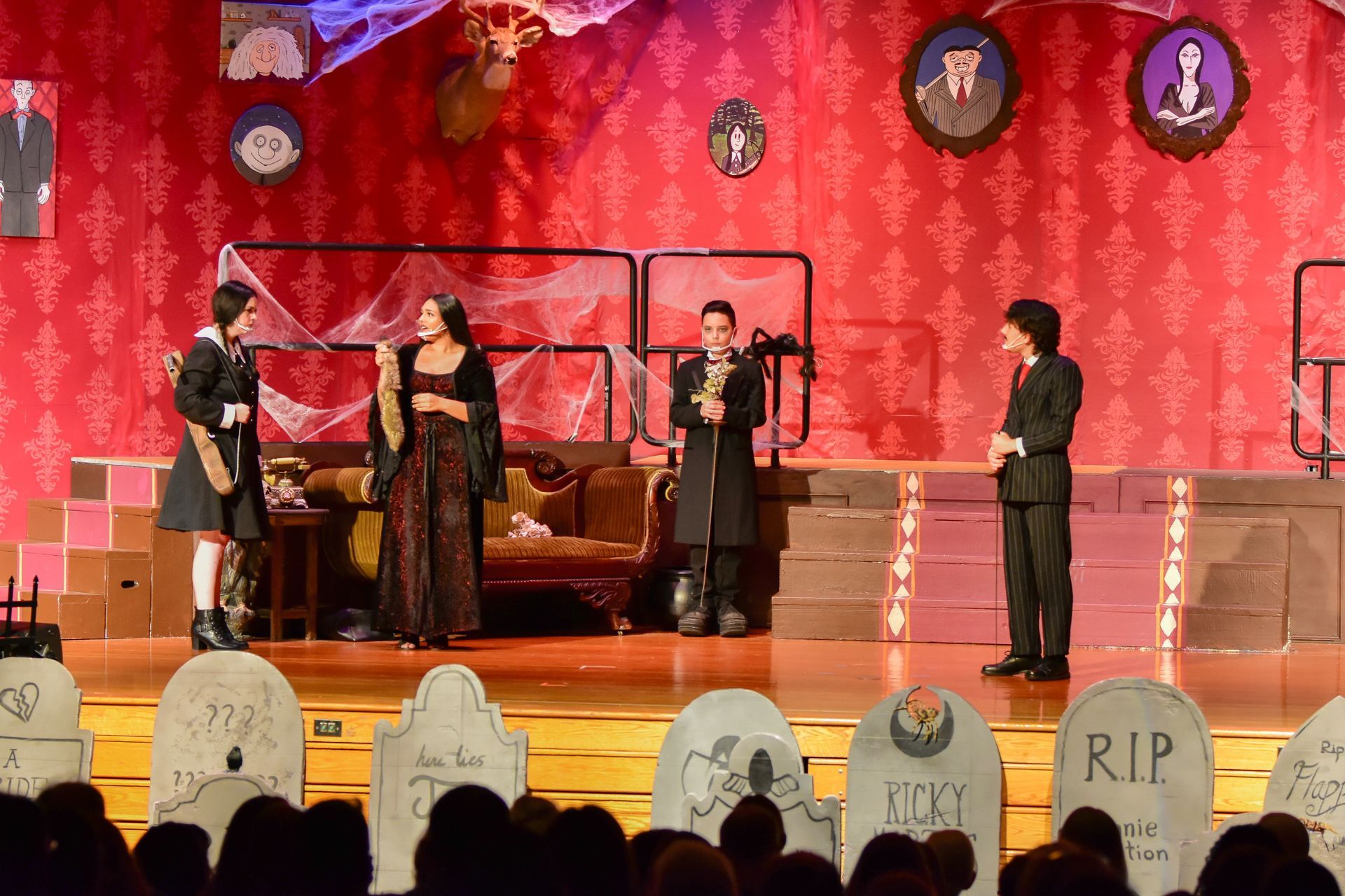 A stage play scene with actors in costume, set with tombstones.
